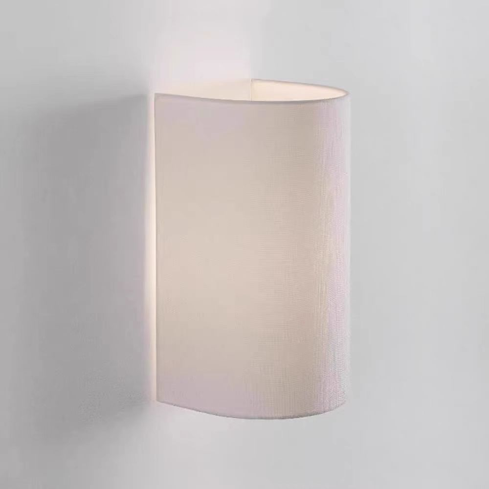 Eine weiße, halb zylindrische Wandleuchte ist an einer weißen Wand befestigt. Sie strahlt ein weiches Licht aus und erzeugt ein sanftes Ambiente.