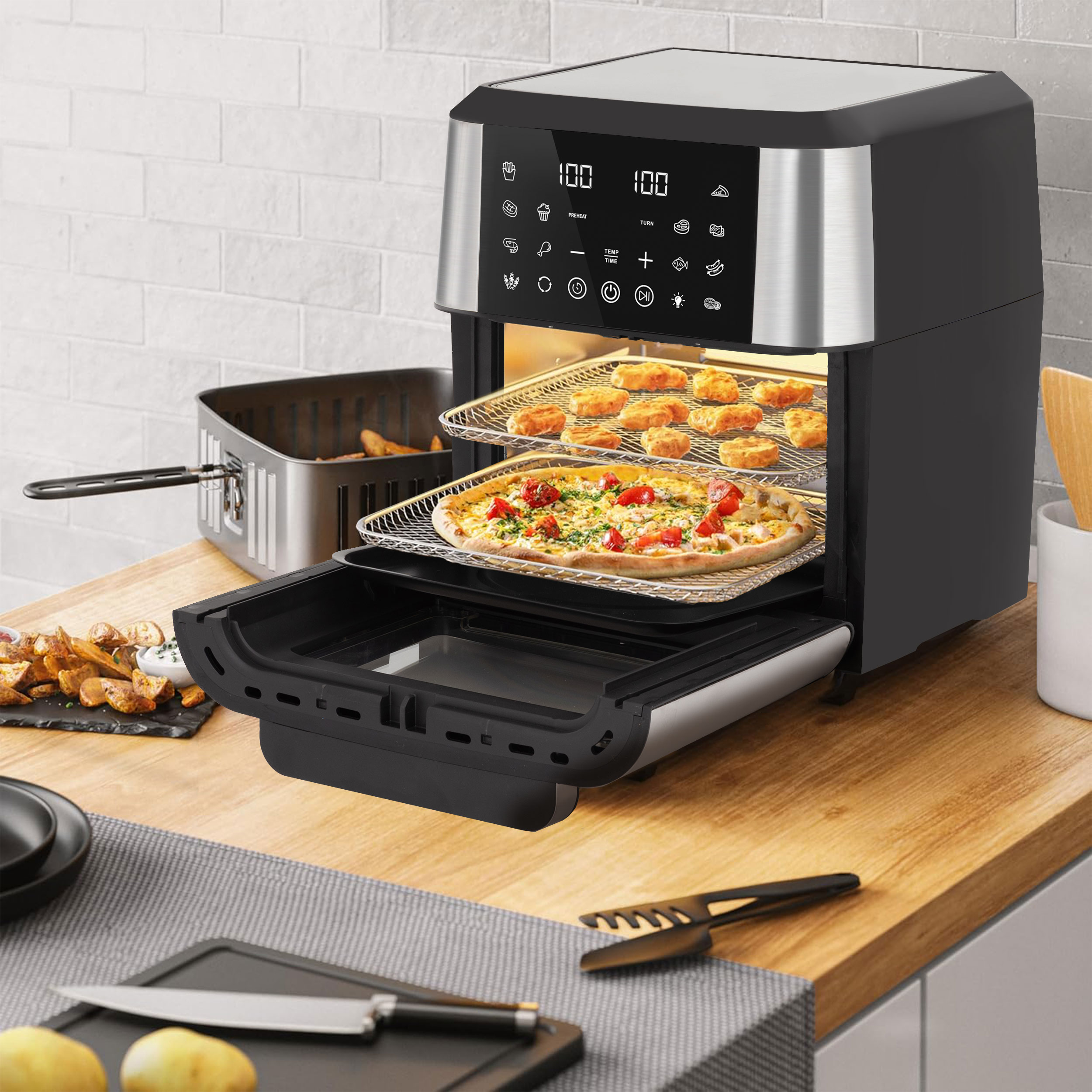 Ein Airfryer mit Essen, plus Pizza. Ein Schneidebrett mit Messer. Kartoffeln, Pommes Frites und eine weiße Backsteinmauer.