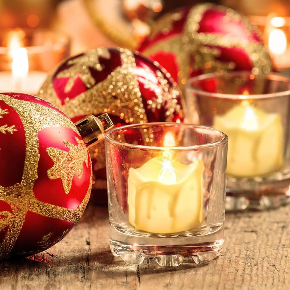 Rote und goldene Weihnachtskugeln, brennende Kerzen in Glashaltern und eine Holzoberfläche schaffen eine warme, festliche Urlaubsszene.