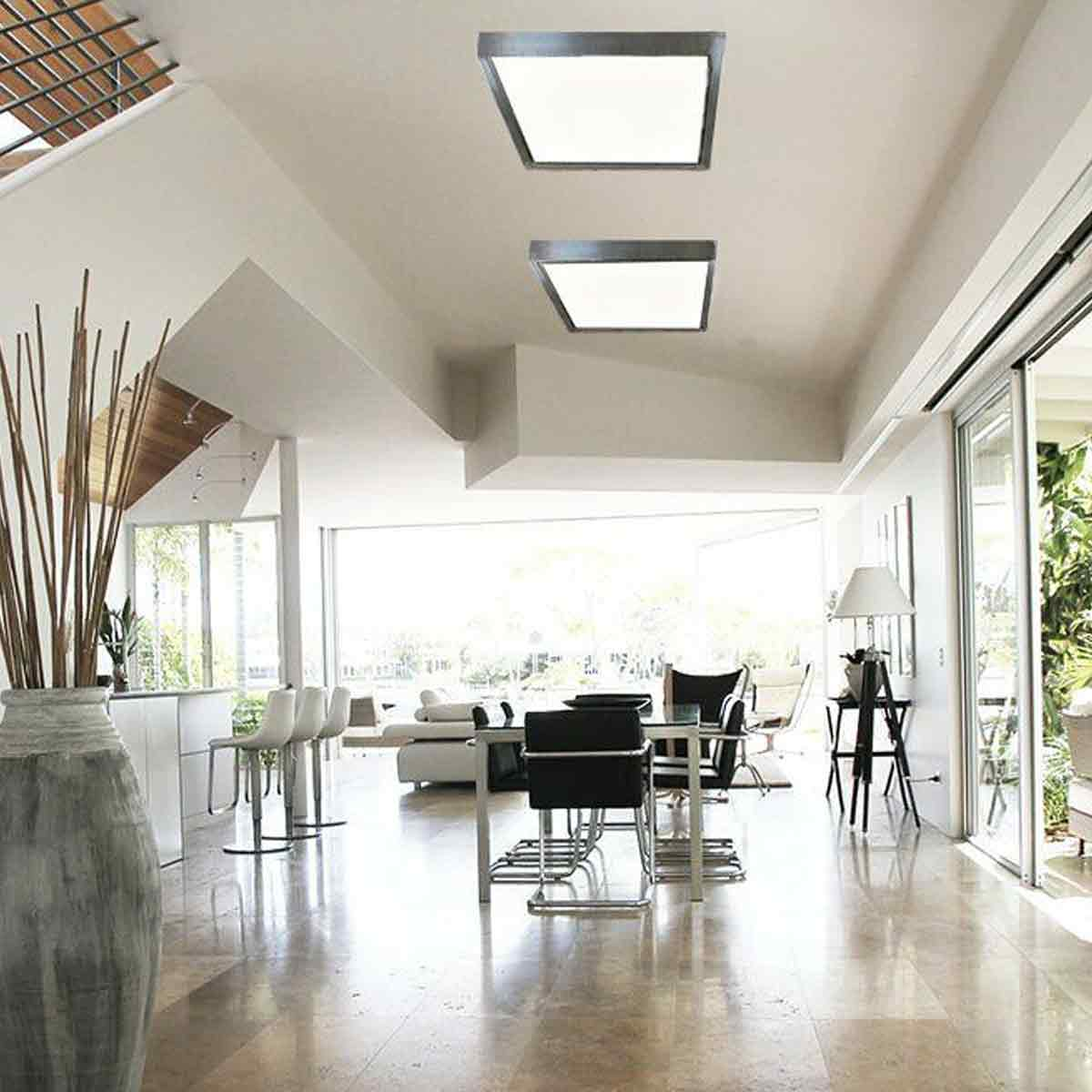 Helles, modernes Wohnzimmer mit zwei Deckenleuchten. Es gibt einen Esstisch, Stühle, eine große Vase und Glastüren zum Garten.
