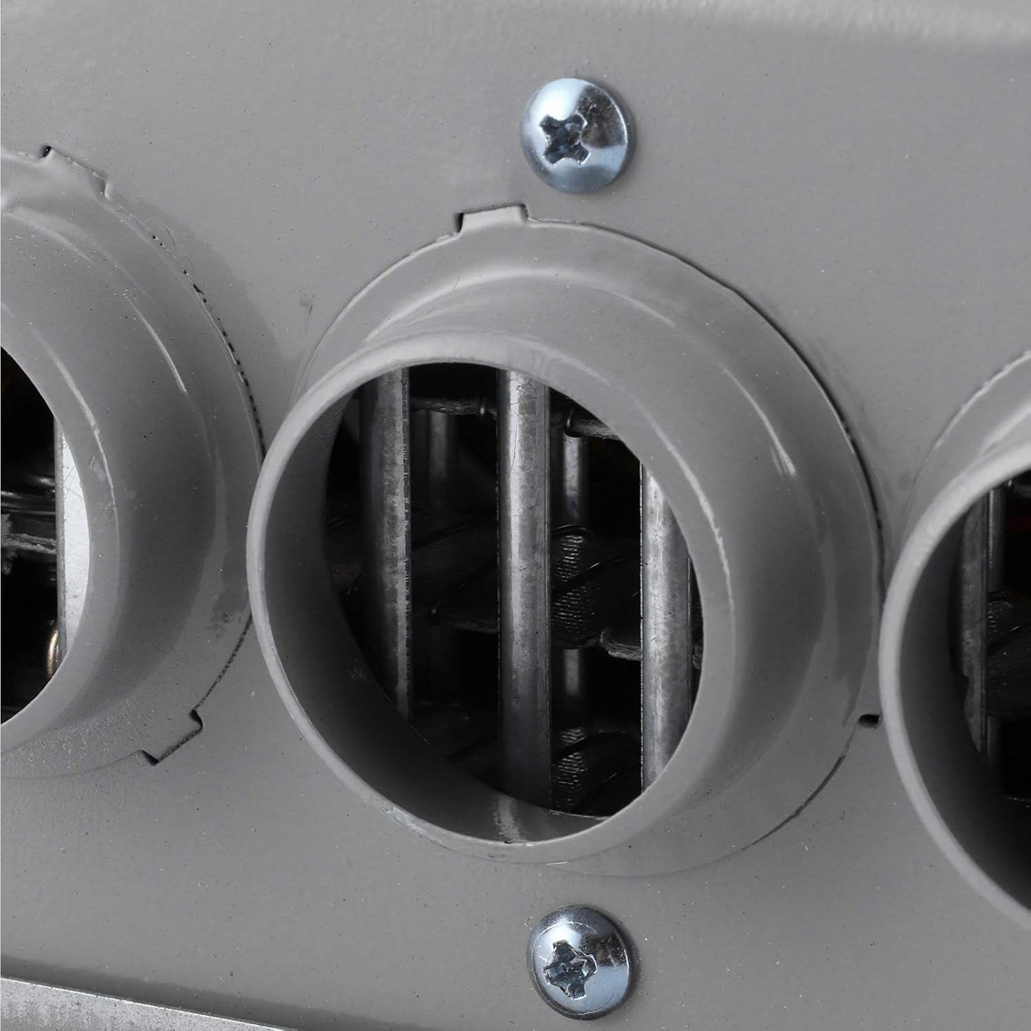 Nahaufnahme eines grauen Metallobjekts. Drei runde Lüftungsöffnungen mit Metallstangen im Inneren. Zwei Schrauben sind sichtbar.