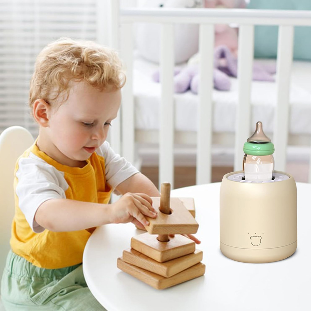 Ein kleines Kind spielt mit einem Holzsteckspielzeug am Tisch. Ein Flaschenwärmer mit Babyflasche steht daneben. Im Hintergrund ist ein Kinderbett.