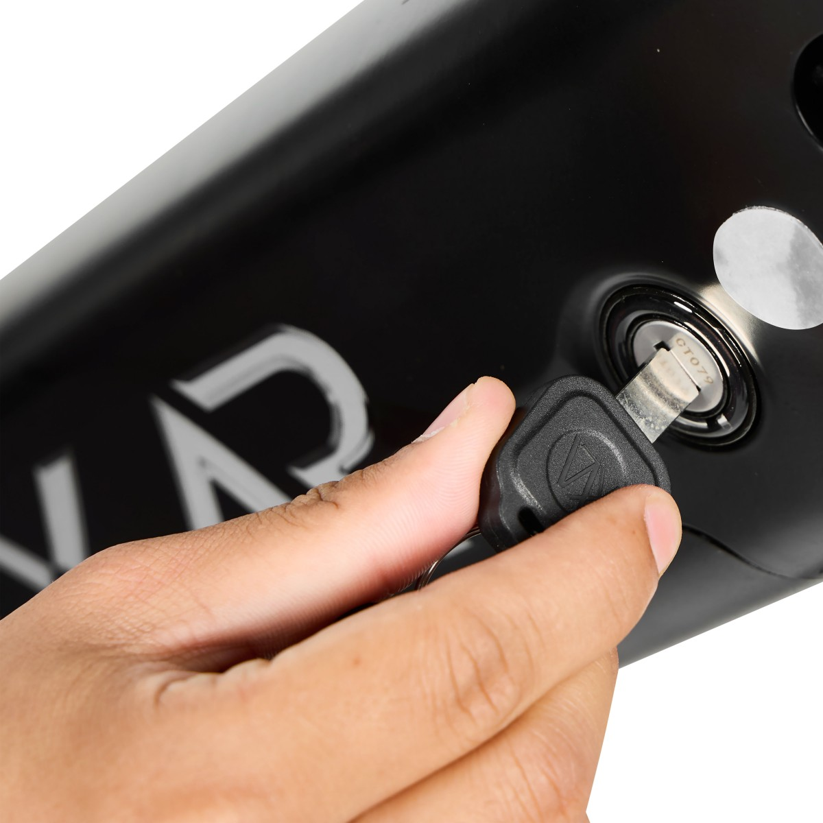 Ręka wkłada klucz do czarnego zamka. Klucz jest czarny, zamek okrągły, a tło to czarna powierzchnia.