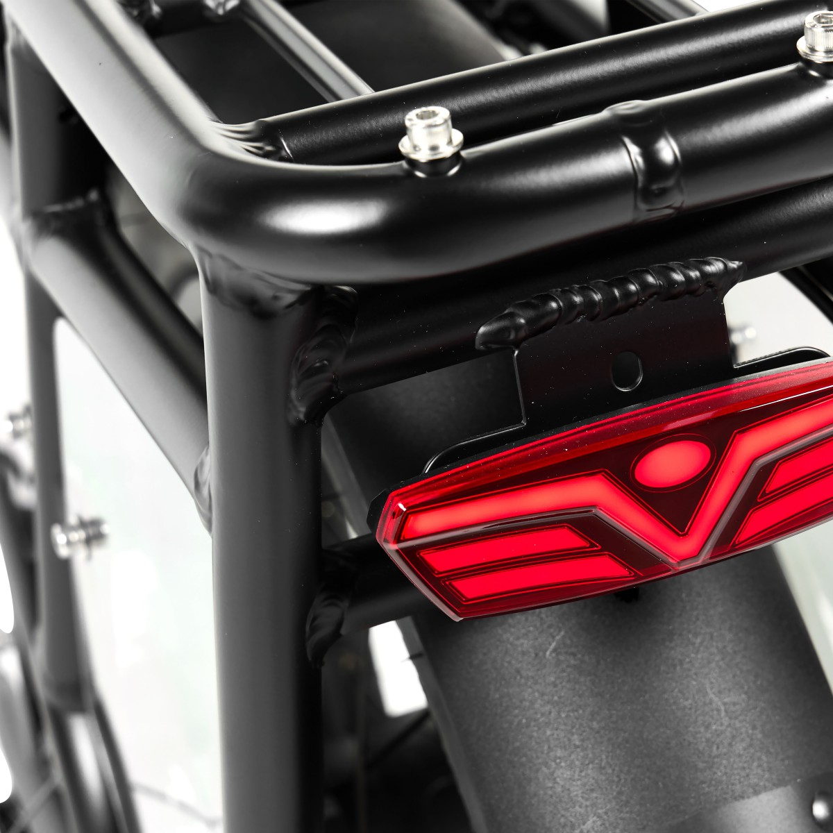 Zbliżenie czarnego bagażnika rowerowego z czerwonym tylnym światłem. Bagażnik ma śruby i jest przymocowany do tylnego błotnika.