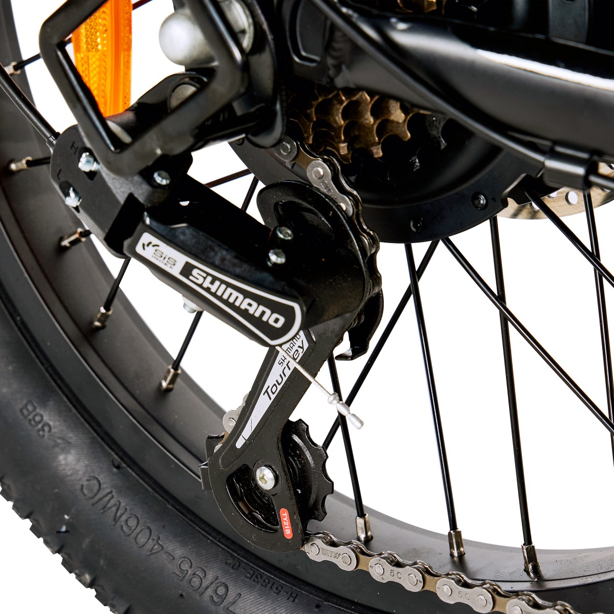 Zbliżenie tylnego koła roweru. Widoczne elementy to przerzutka Shimano, łańcuch, zębatki, opona i szprychy.