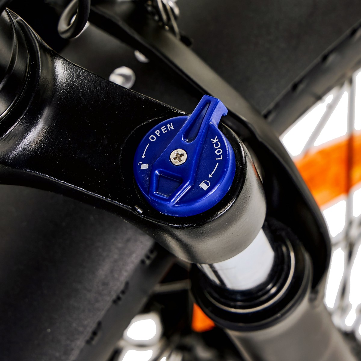 Zbliżenie widelca amortyzowanego roweru. Niebieska tarcza wskazuje 'otwarte' i 'zablokowane'. Czarne metalowe części dominują widok.