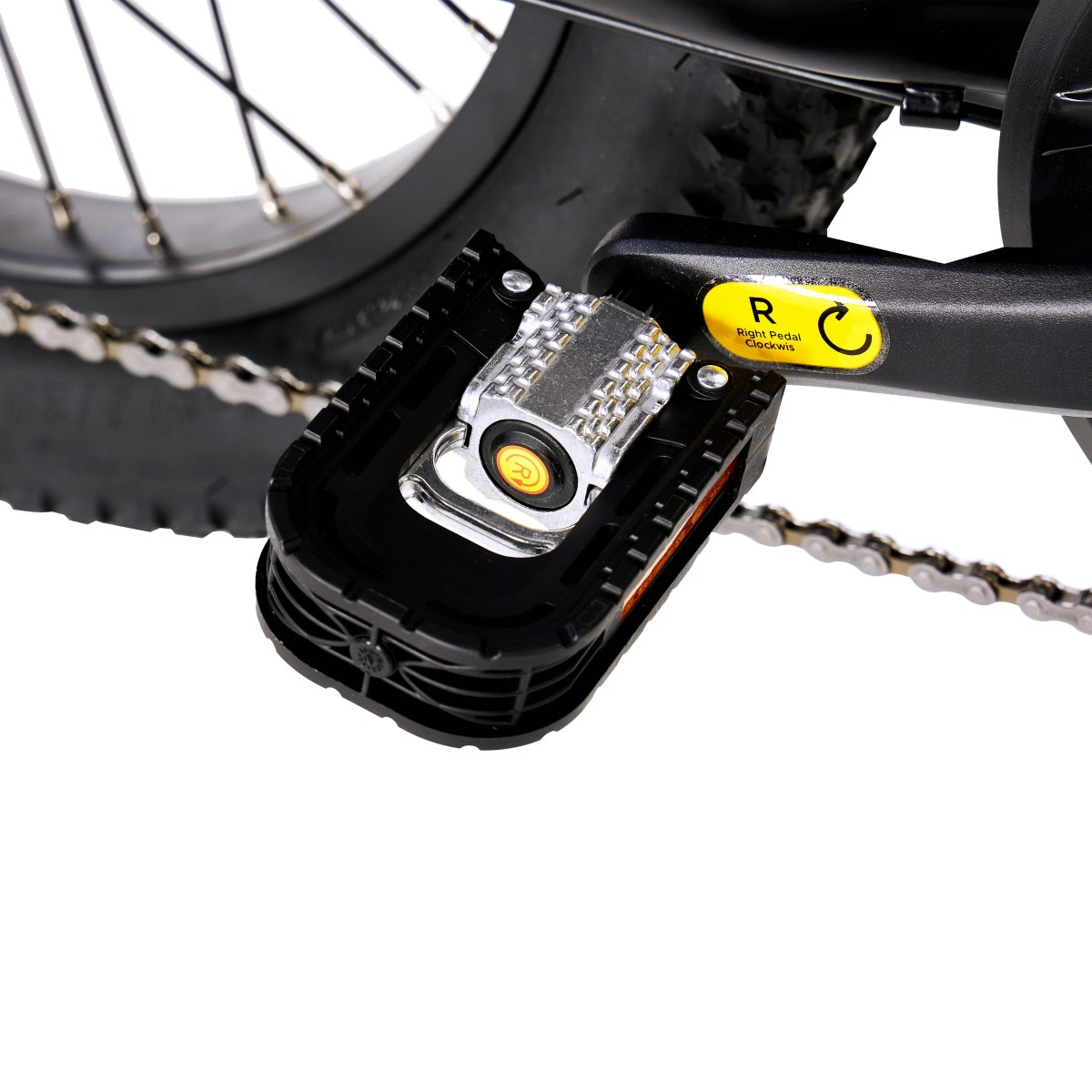 Zbliżenie pedału roweru. Czarny pedał ma srebrny środek i żółtą naklejkę wskazującą prawą stronę.