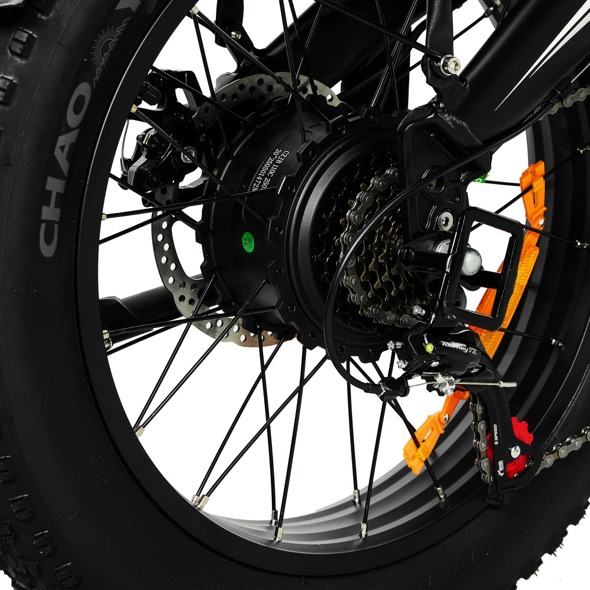 Zbliżenie czarnego koła roweru z grubą oponą. Widoczne łańcuch, zębatki, hamulec tarczowy i pomarańczowe odblaski.