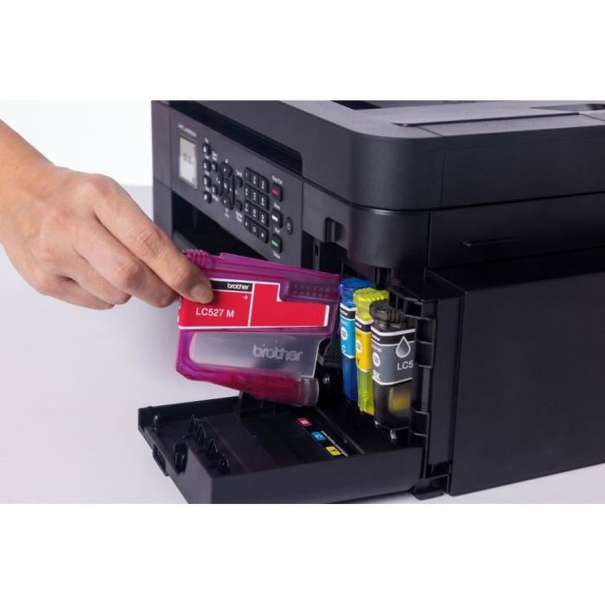 Dłoń wkładająca magentowy wkład atramentowy do czarnej drukarki Brother. Widoczne są inne wkłady kolorowe.