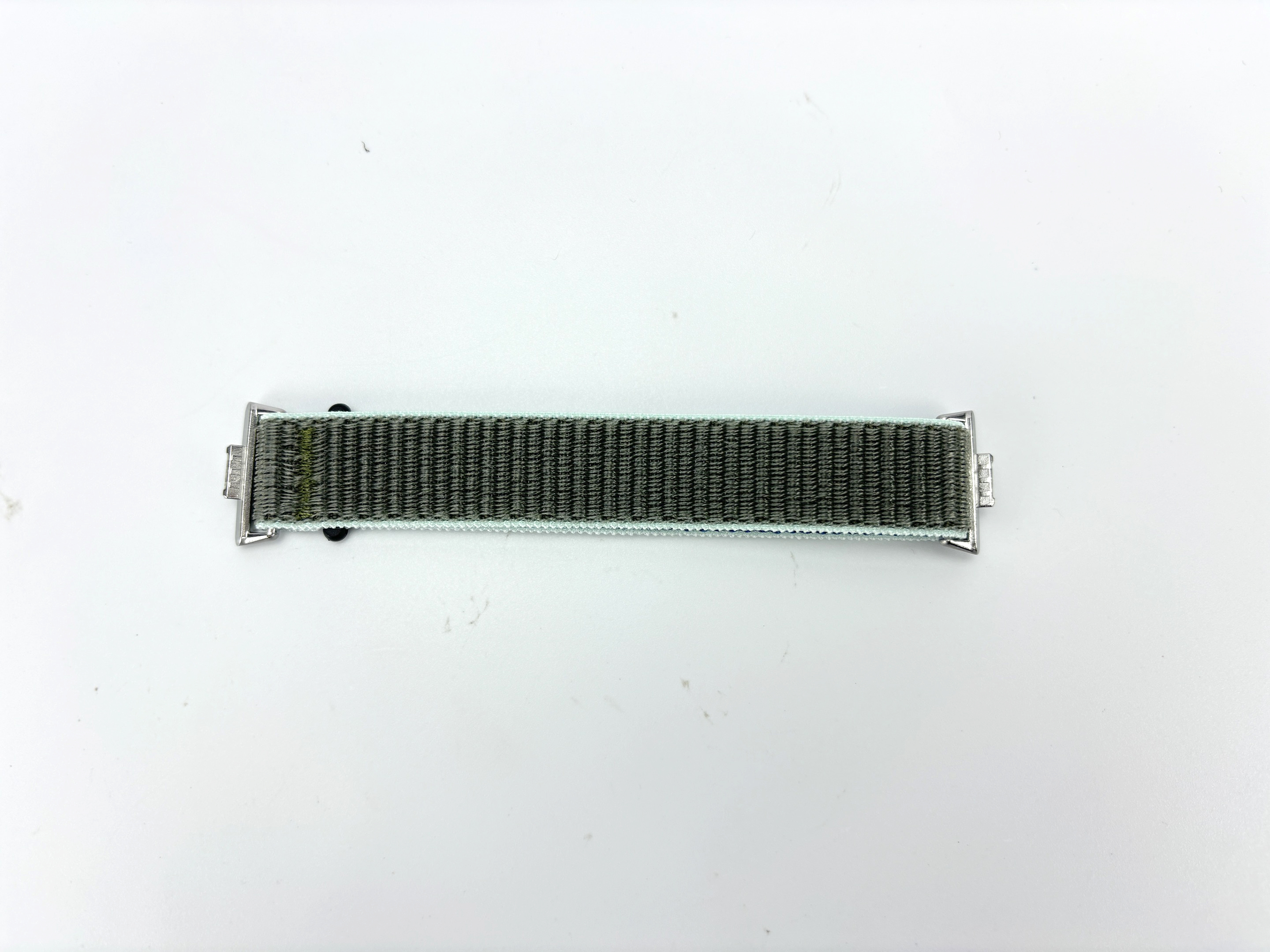 Ein Uhrenarmband liegt mittig auf einer weißen Oberfläche. Es ist grau mit hellgrünen Rändern und silbernen Verschlüssen.
