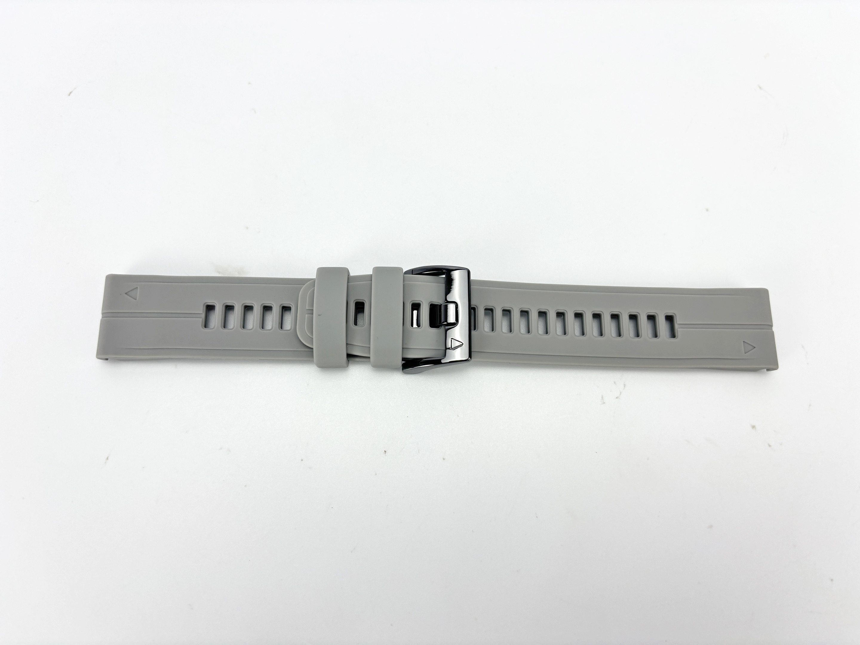 Ein graues Armband liegt auf einer weißen Oberfläche. Es hat eine Schnalle und mehrere Löcher.