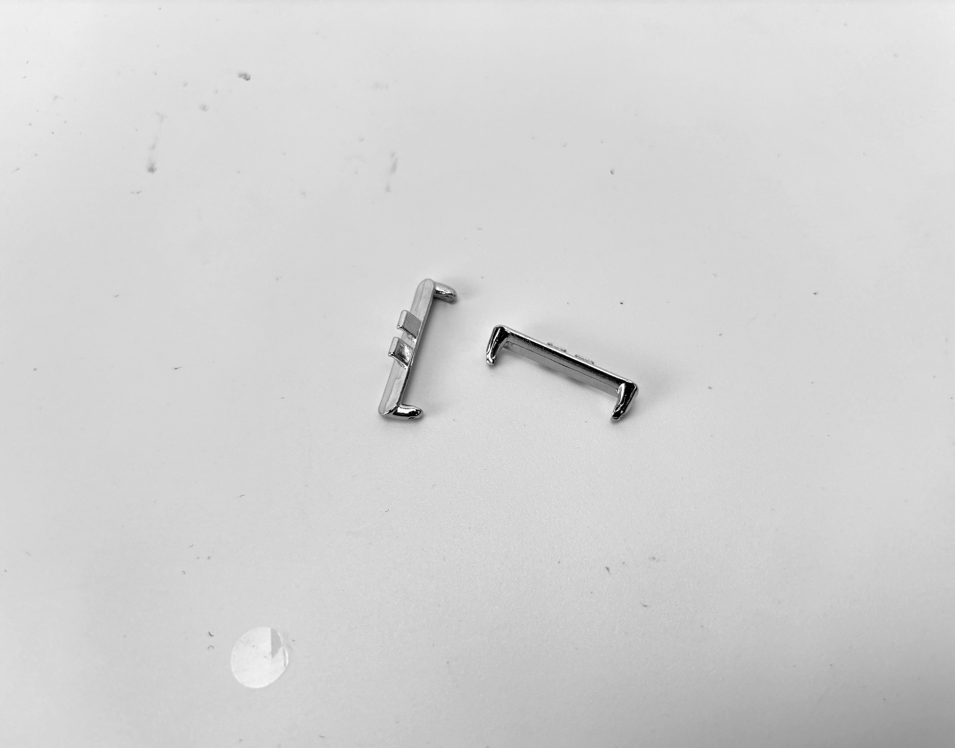 Due piccoli oggetti metallici lucenti su una superficie bianca. Uno è in posizione verticale, l'altro è sdraiato. La superficie presenta dei segni.