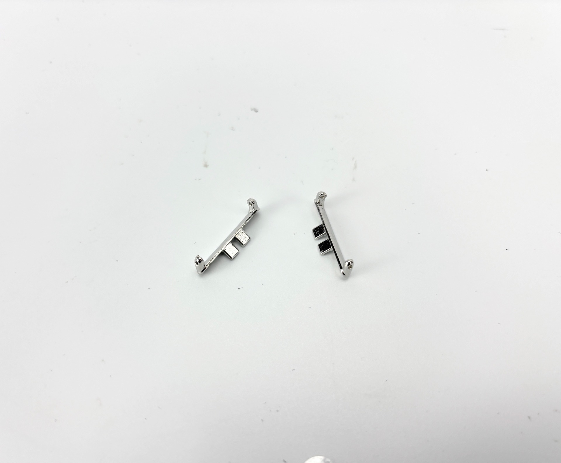 Due piccoli pezzi di metallo argentato su una superficie bianca. Ognuno ha estremità arrotondate e un intaglio rettangolare.