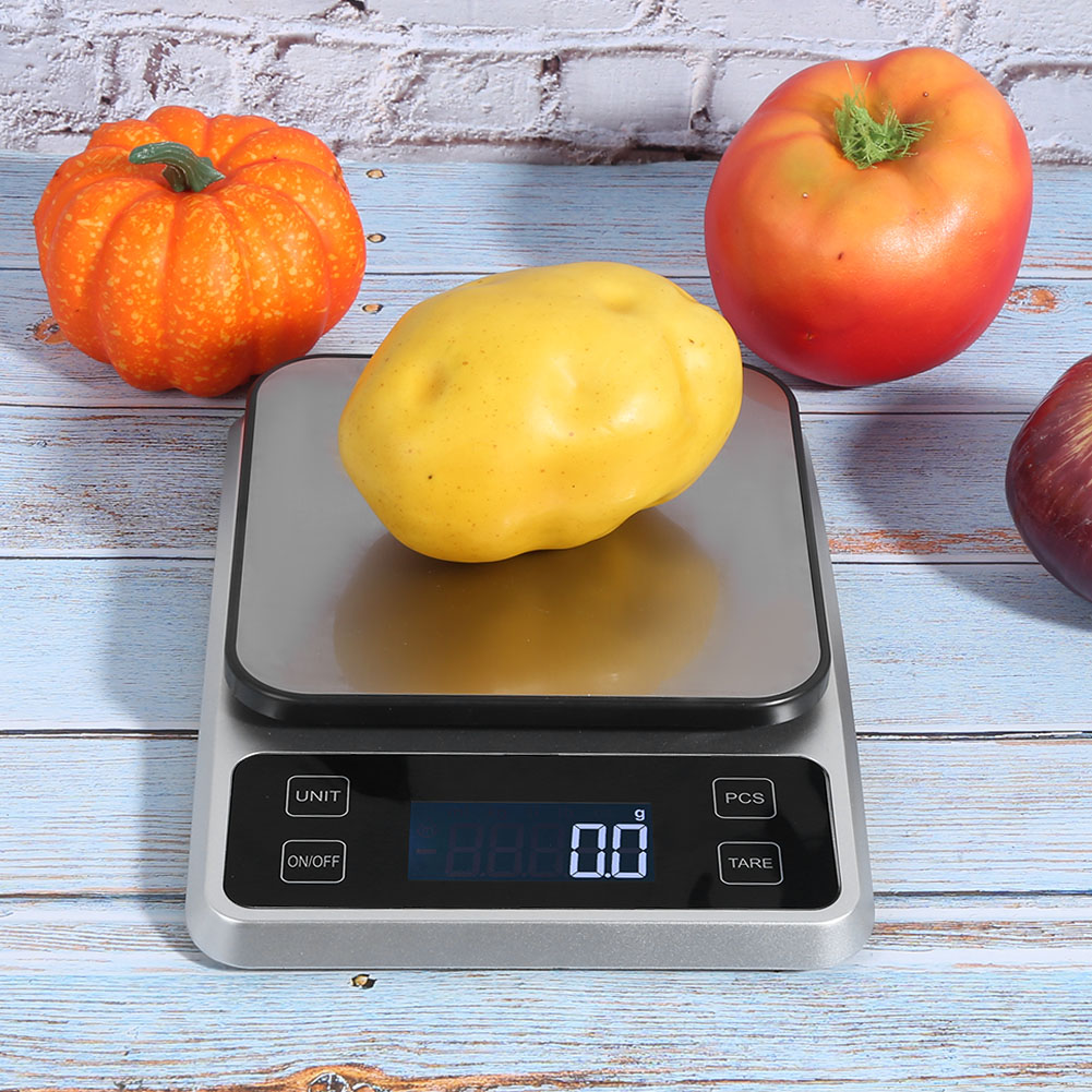 Eine Kartoffel liegt auf einer Digitalwaage, die 0,0 g anzeigt. Ein oranger Kürbis, eine rote Tomate und eine rote Zwiebel sind drumherum.