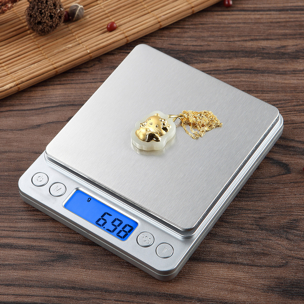 Eine Digitalwaage zeigt 6,98g an. Ein goldener Anhänger liegt darauf. Der Hintergrund umfasst eine Holzoberfläche und eine Bambusmatte.