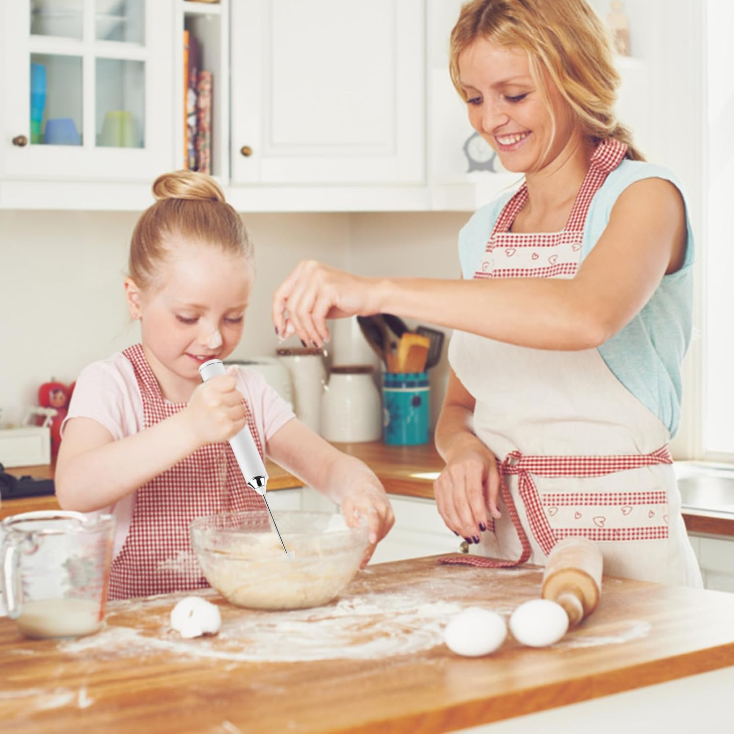 Eine Frau und ein Mädchen backen in einer Küche. Das Mädchen benutzt einen Mixer, während die Frau Mehl streut.