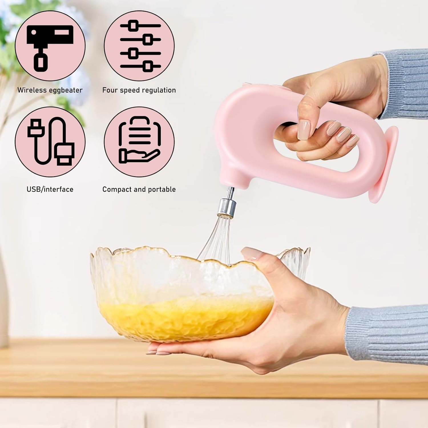 Ein rosa Handmixer verrührt Eier in einer Glasschüssel. Vier Symbole zeigen Funktionen wie USB und Geschwindigkeitsregelung.