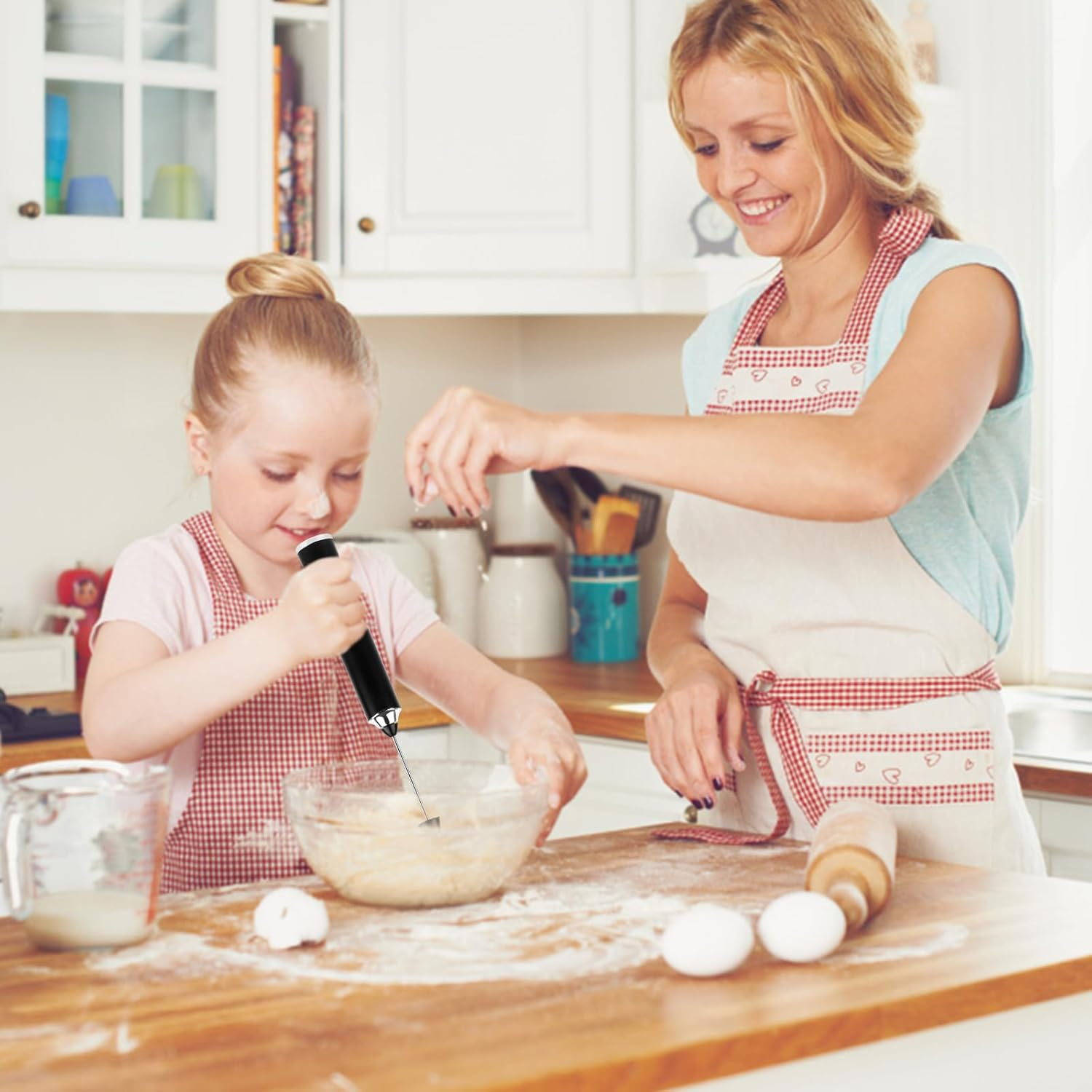 Eine Frau und ein Kind backen. Das Kind verrührt Teig mit einem Handmixer. Die Frau lächelt und gibt Zutaten hinzu.