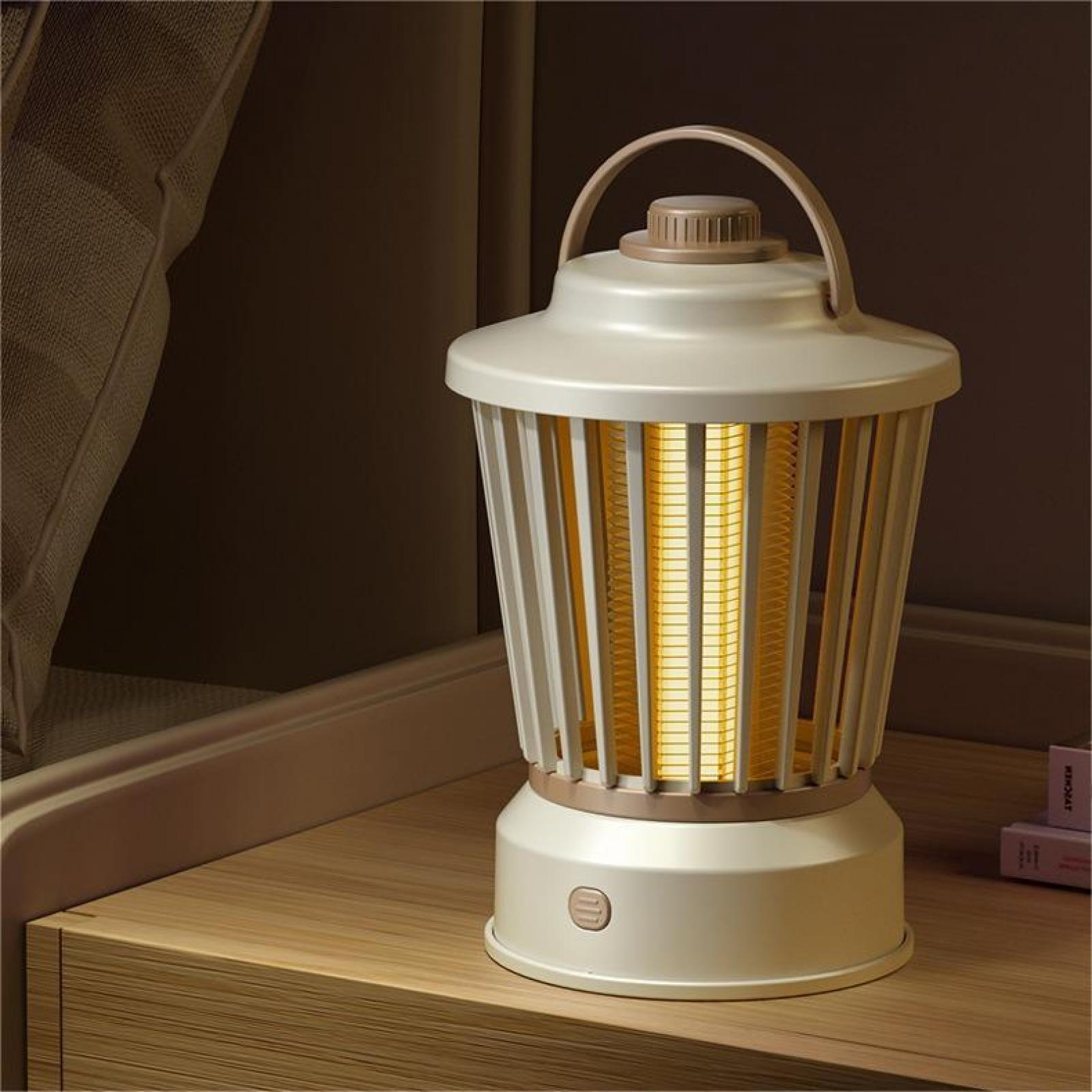 Cremefarbene Lampe mit Griff auf Holzoberfläche. Dahinter ein Bett und eine Wand. Die Lampe strahlt warmes Licht aus.