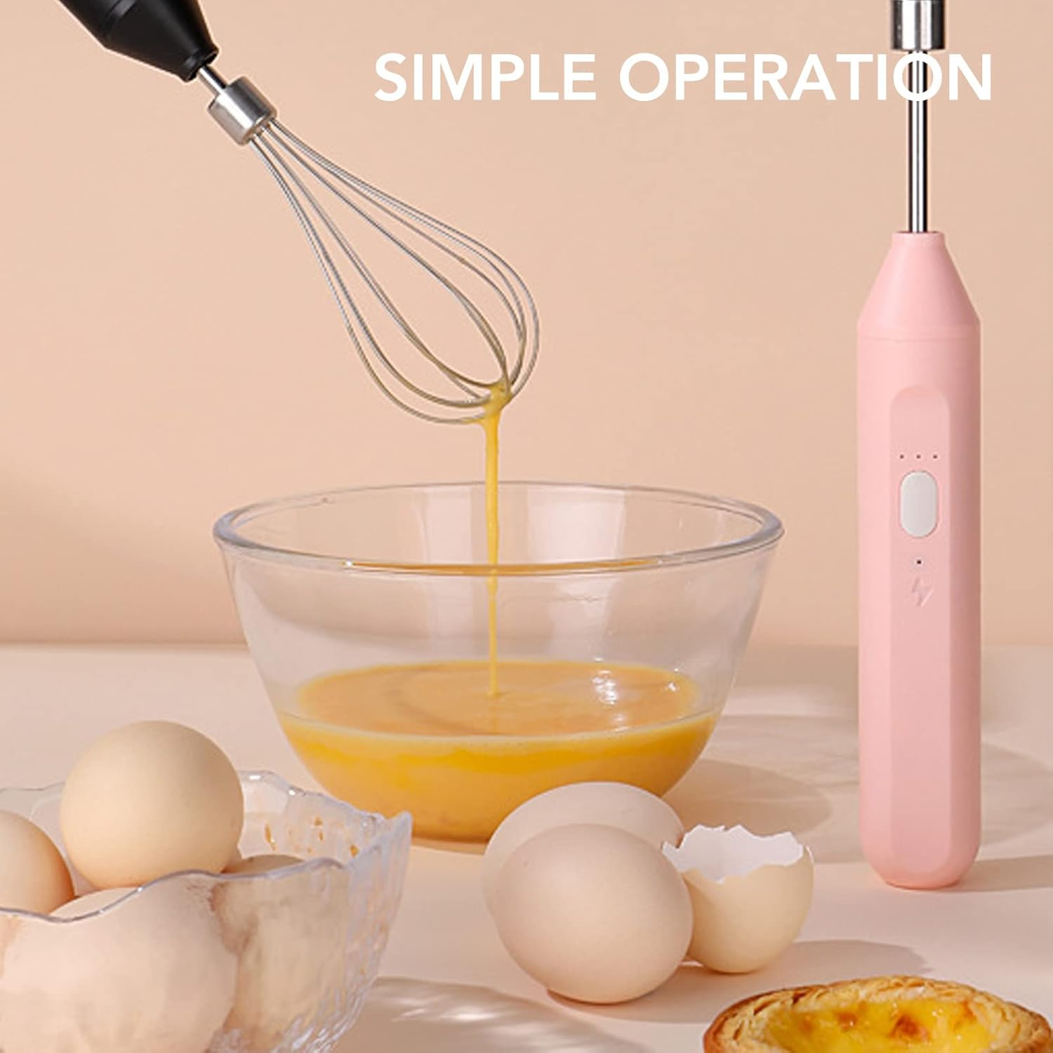 Ein Schneebesen verrührt Eier in einer Schüssel. Ein rosa Handmixer ist in der Nähe. Eier und Gebäck liegen auf dem Tisch.