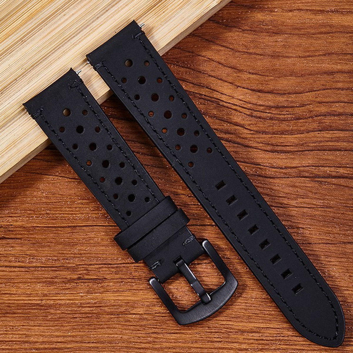 Schwarze Armbänder mit Löchern und einer Schnalle liegen auf einer Holzoberfläche mit einem kleinen Holzblock.