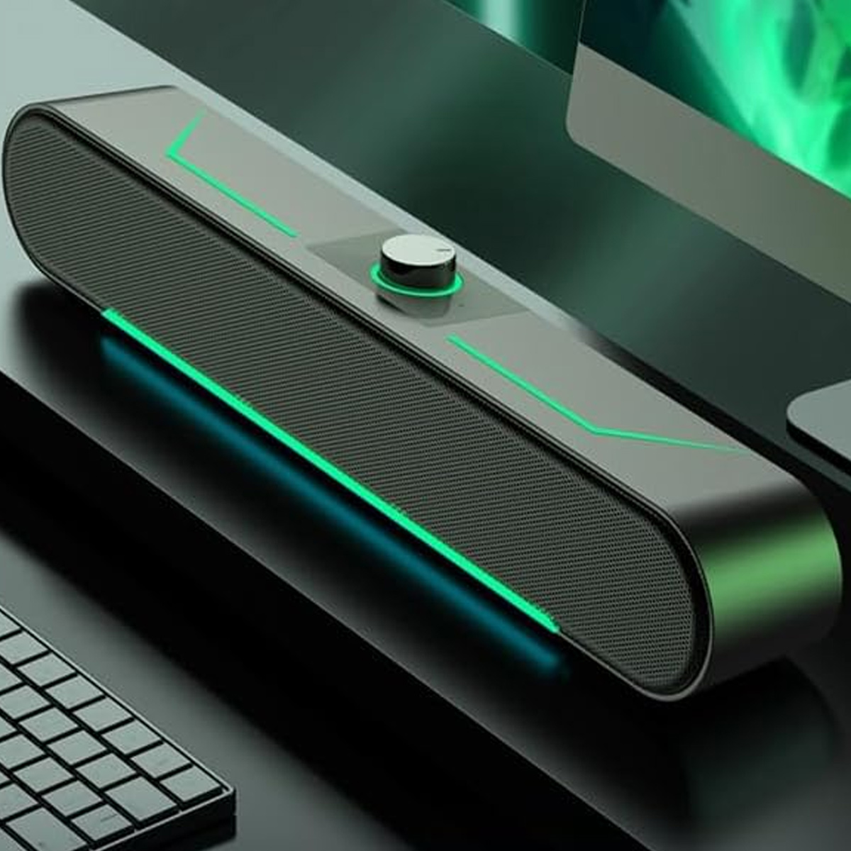 Ein dunkler Lautsprecher mit grünen Akzenten und einem Lautstärkeregler. Im Hintergrund befinden sich eine Tastatur und ein Monitor.