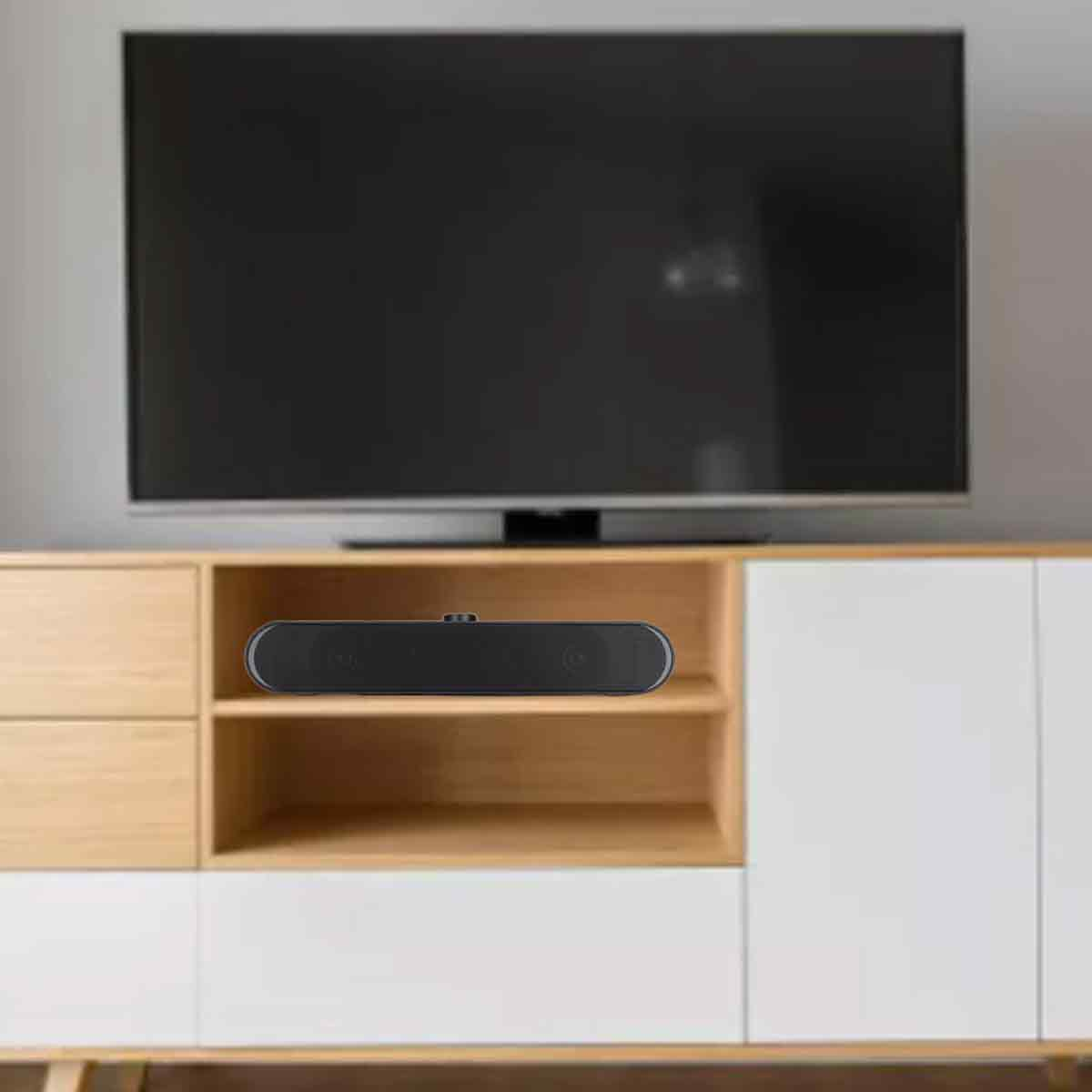Eine schwarze Soundbar steht auf einem Holzregal unter einem großen, schwarzen Fernseher. Der Schrank hat weiße und Holztüren.