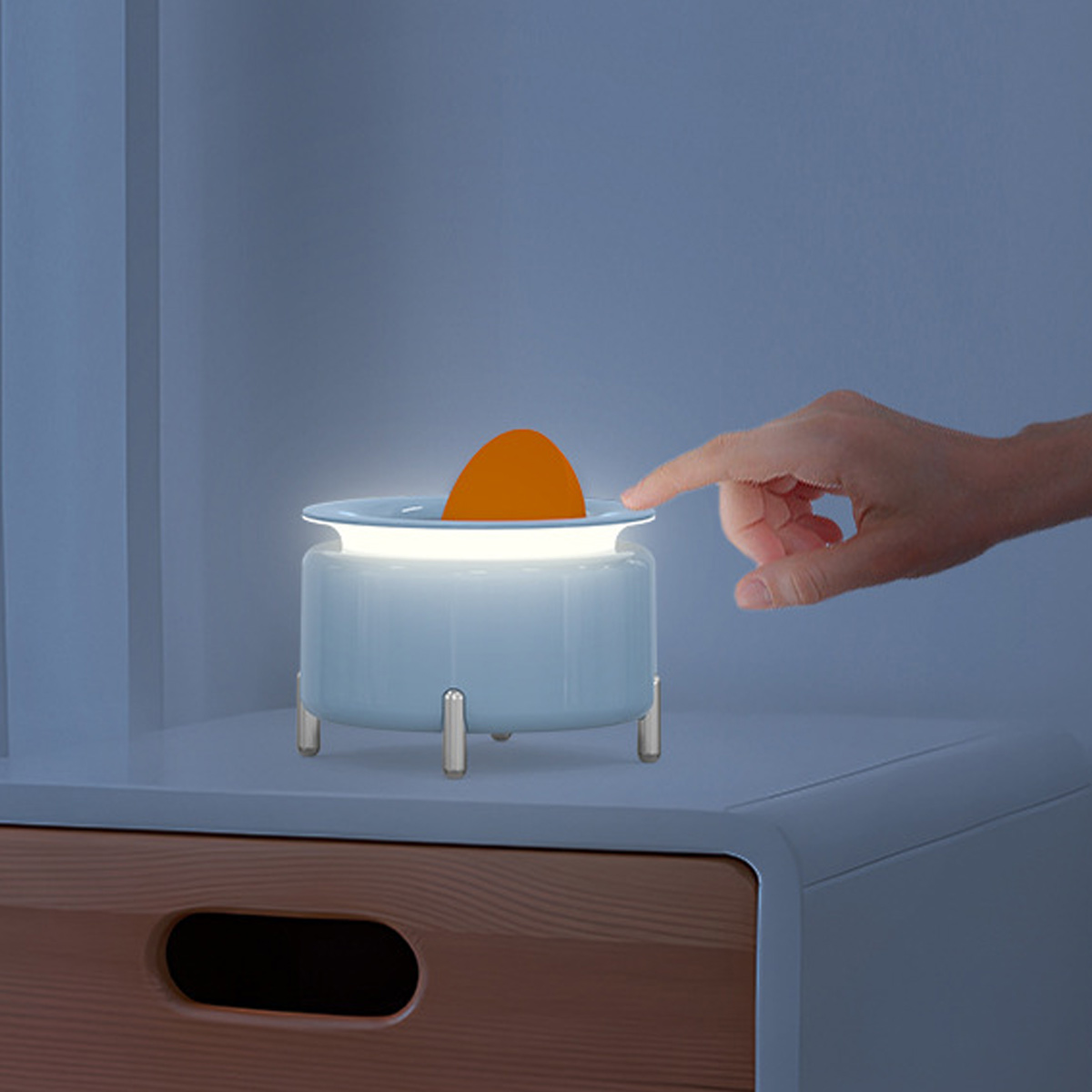 Eine Hand berührt eine blau-weiße Lampe mit einem orangefarbenen Objekt. Die Lampe steht auf einem Nachttisch.