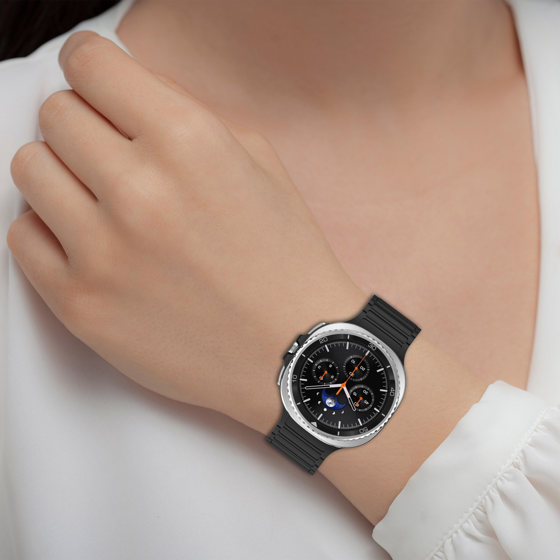 Una persona indossa uno smartwatch nero con lunetta argentata. Il braccio è appoggiato su una camicia bianca. Tono della pelle chiaro.