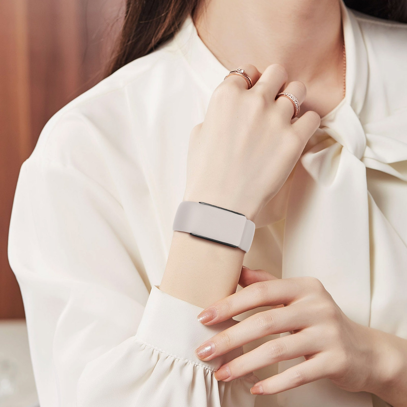 Eine Person trägt Ringe und ein weißes Hemd mit einem weißen Smart-Armband am Handgelenk.