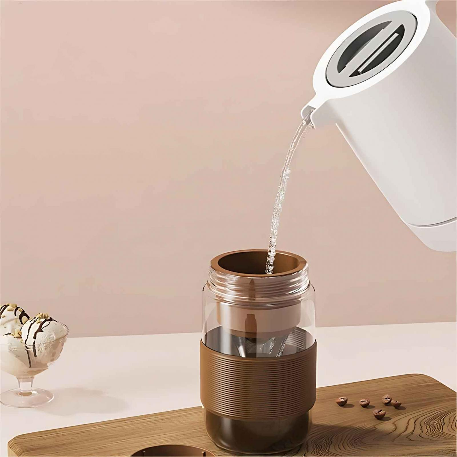 Ein weißer Wasserkocher gießt Wasser in eine braune Kaffeemaschine. Eis und Kaffeebohnen sind ebenfalls sichtbar.