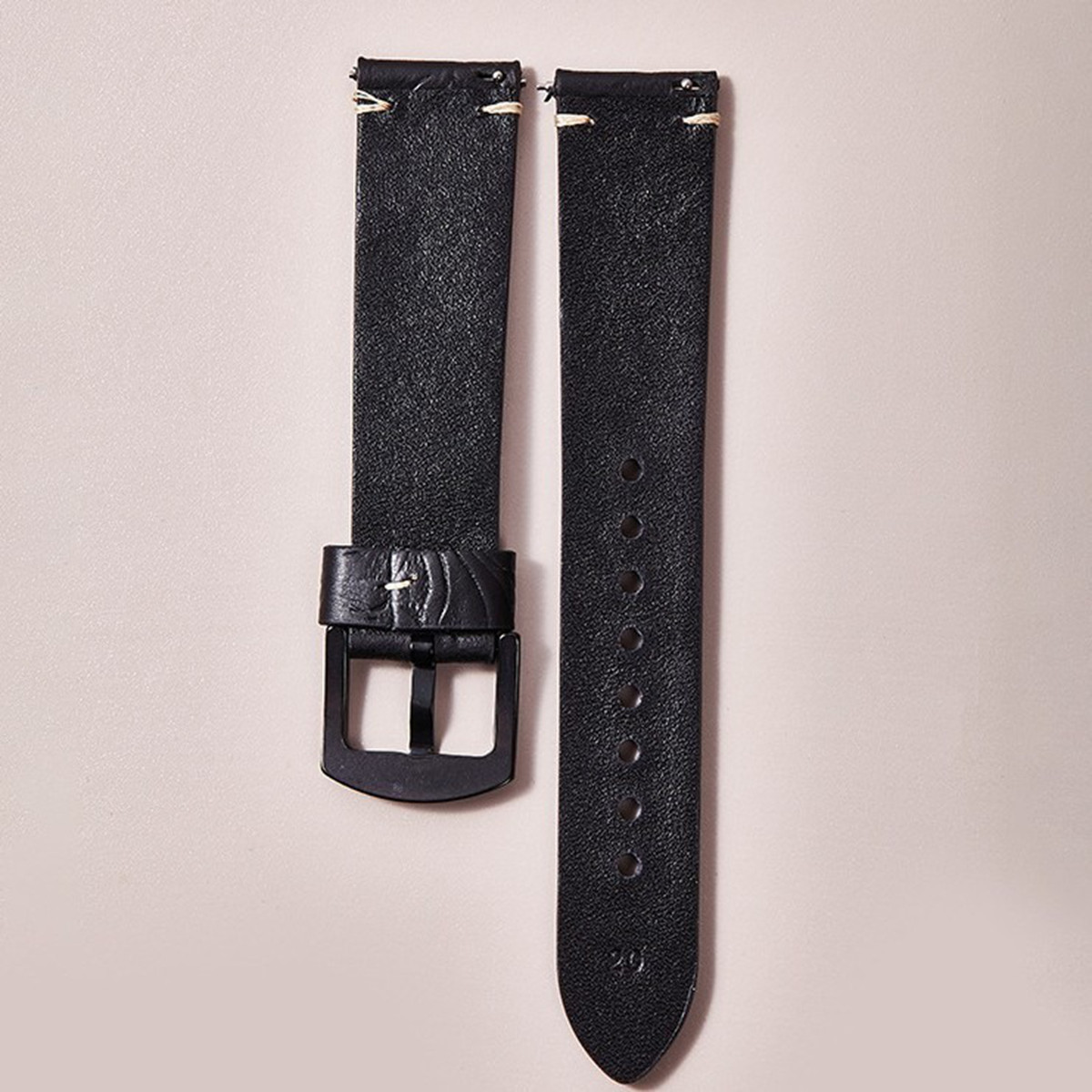 Due cinturini per orologio in pelle nera con cuciture bianche. Uno ha una fibbia. Lo sfondo è beige chiaro.