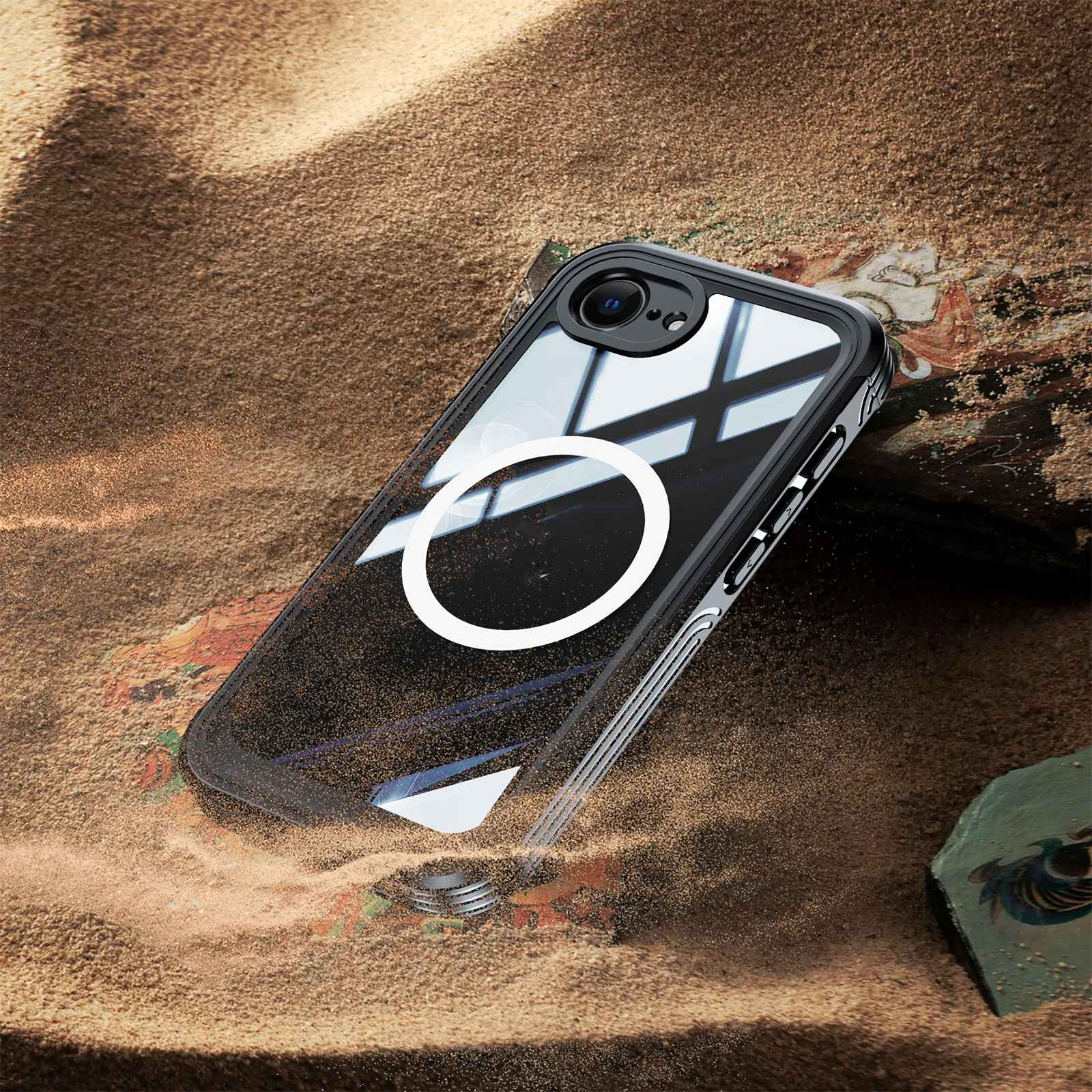Eine klare Handyhülle mit weißem Kreis liegt auf Sand. Die Hülle hat einen schwarzen Rand und eine Kamera. Der Hintergrund ist Sand.