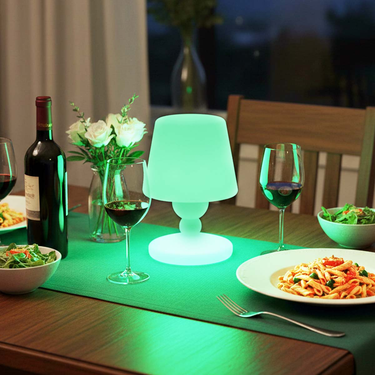 Una tavola apparecchiata con vino, cibo e una lampada luminosa. Include calici, pasta, insalata e fiori, creando un'atmosfera romantica.
