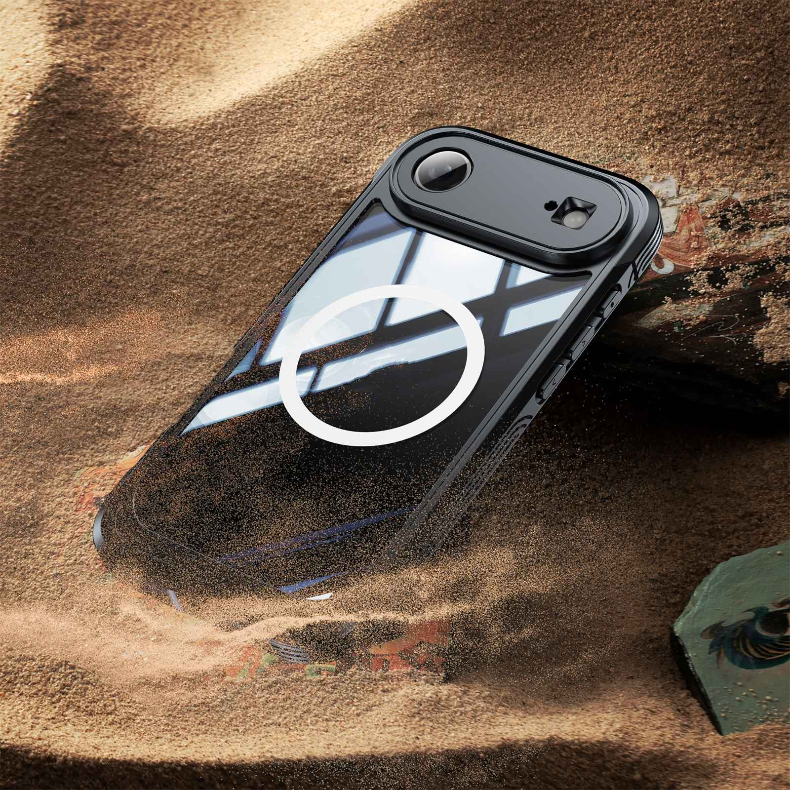 Eine schwarze Handyhülle mit weißem Ring liegt auf Sand. Oben befindet sich ein kleines Kameramodul. Der Hintergrund hat Sand und einen Stein.
