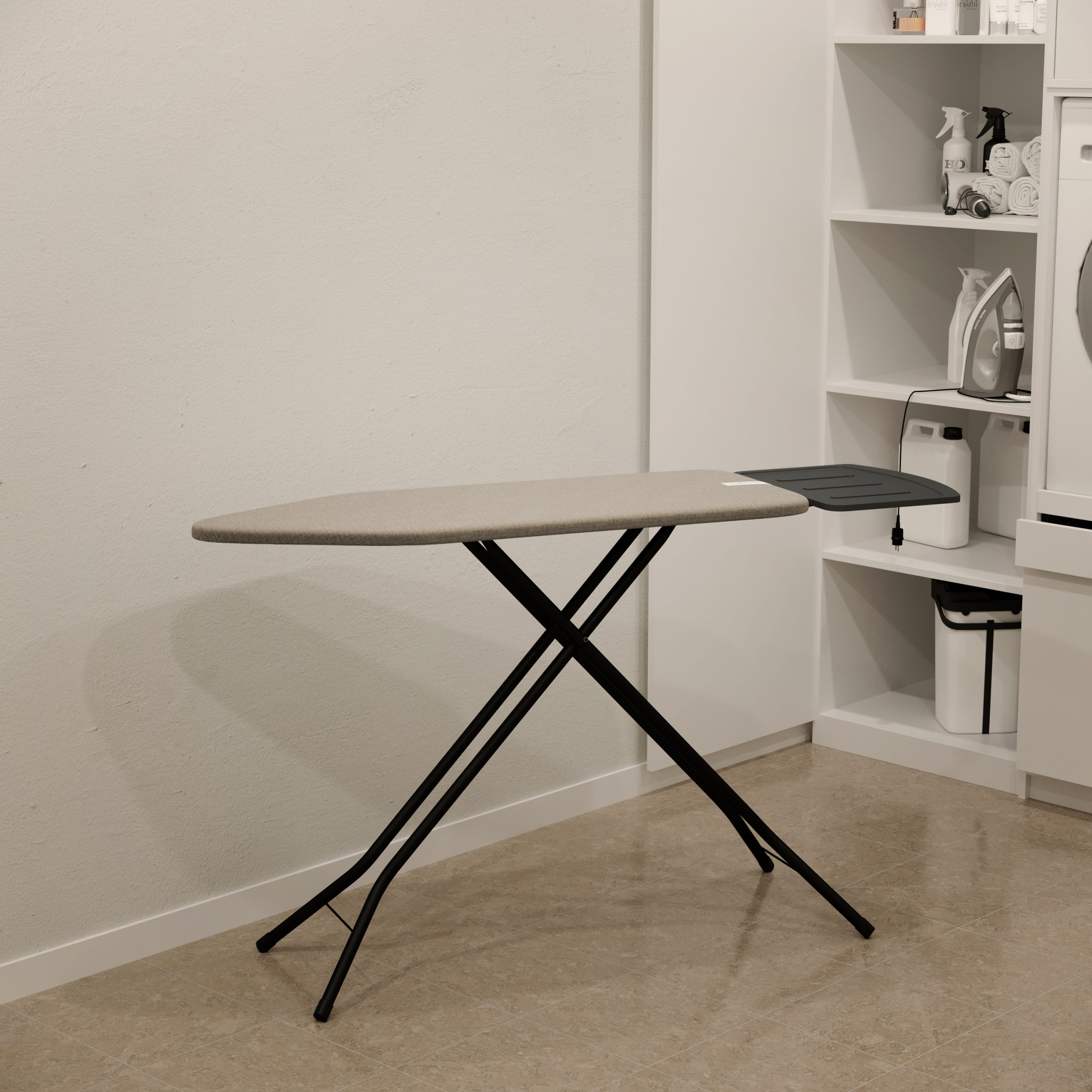 An ironing board in a room. It has a beige top and black legs. A white wall and shelves are in the background.