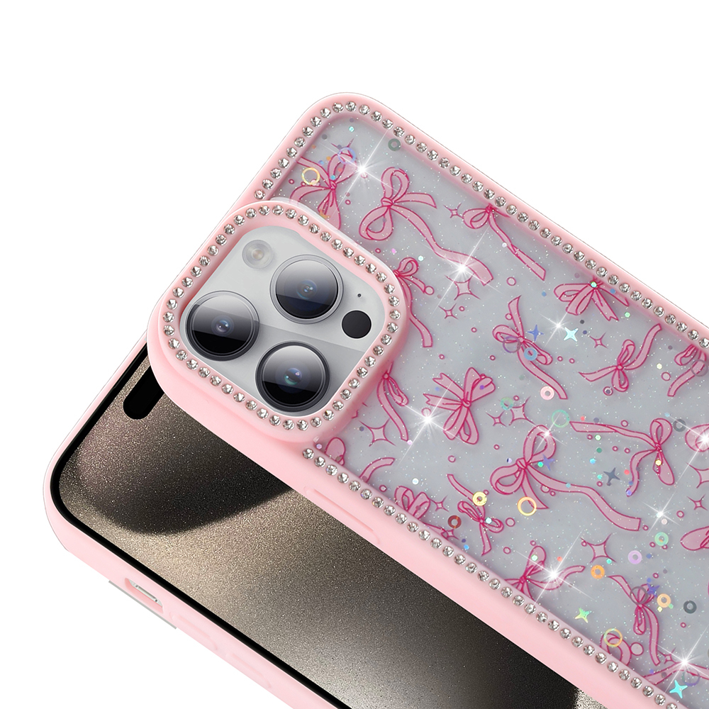 Kurdele desenli ve taşlı pembe bir telefon kılıfı. Telefonun siyah bir ekranı var. Kılıf beyaz bir yüzey üzerinde.