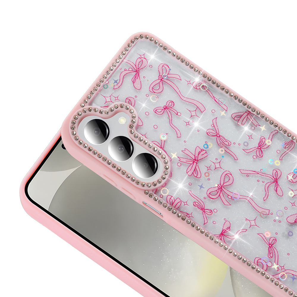 Yay ve parıltılarla pembe telefon kılıfı, kamera çevresinde yapay elmaslar. Telefon kısmen görünür, beyaz bir yüzeyde duruyor.