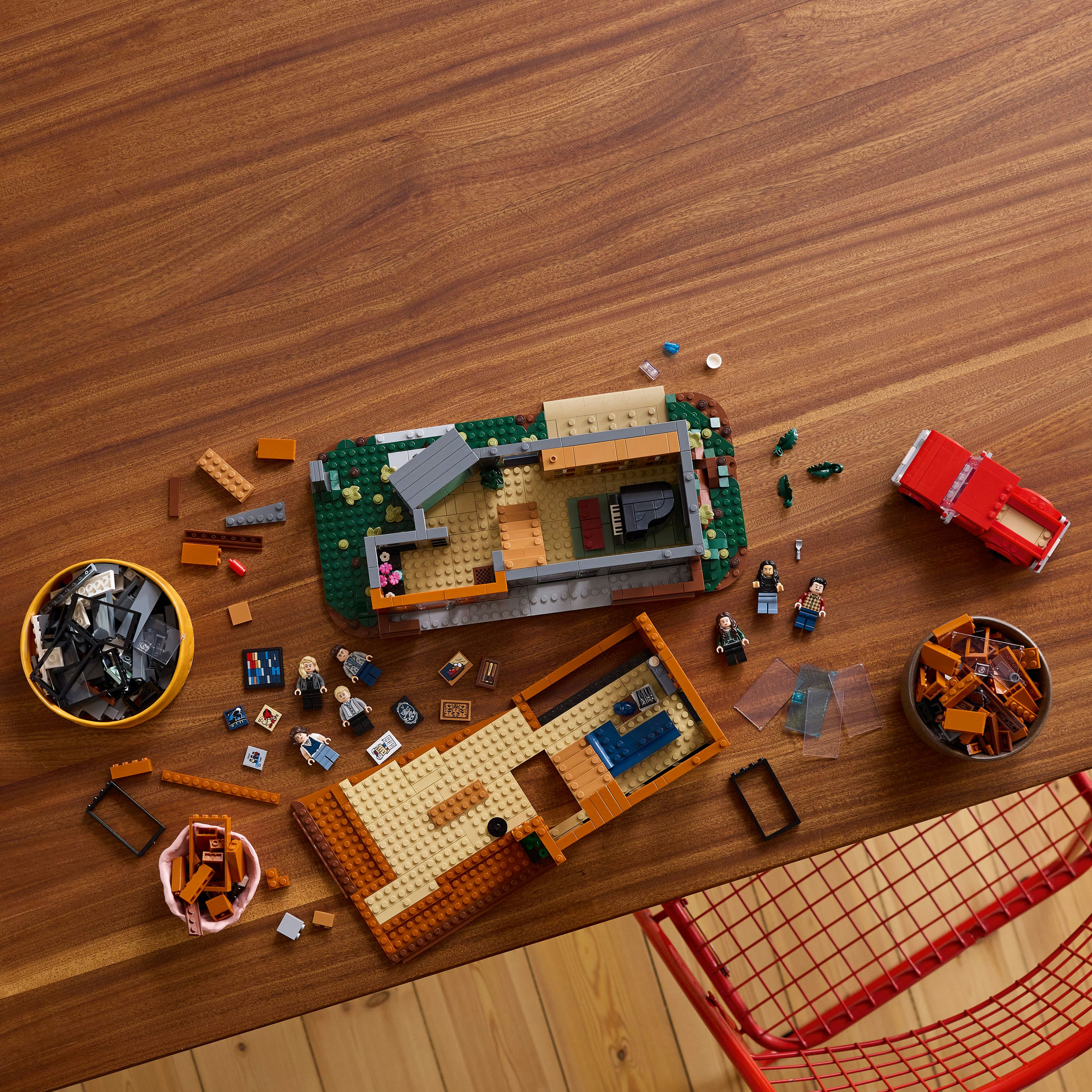 Zestaw LEGO na drewnianym stole. Zawiera dom, samochód, minifigurki i pojemniki z klockami.