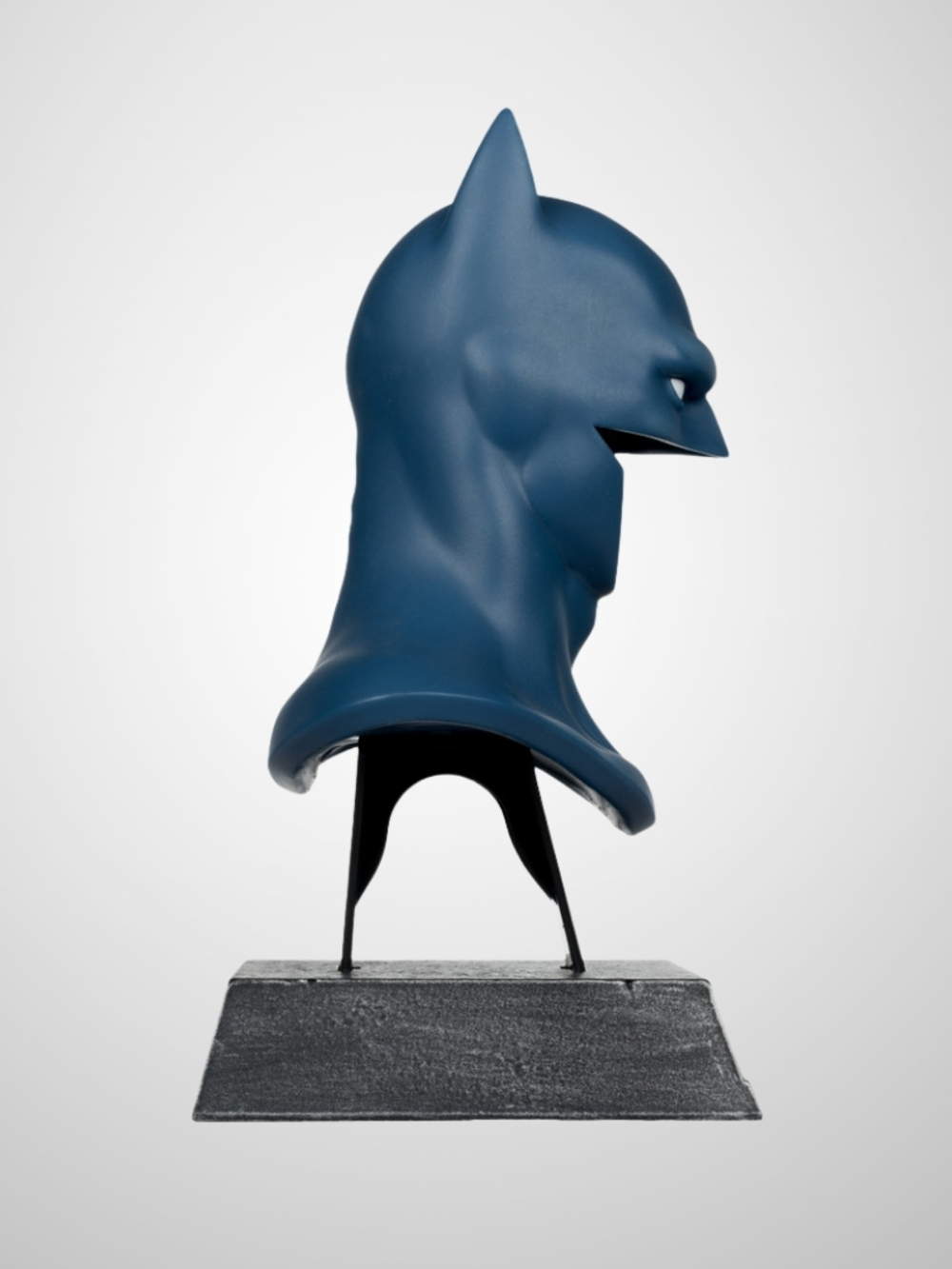 Bir Batman başlığı heykeli. Mavi renkte, bir stand üzerine monte edilmiş. Arka plan düz beyazdır.