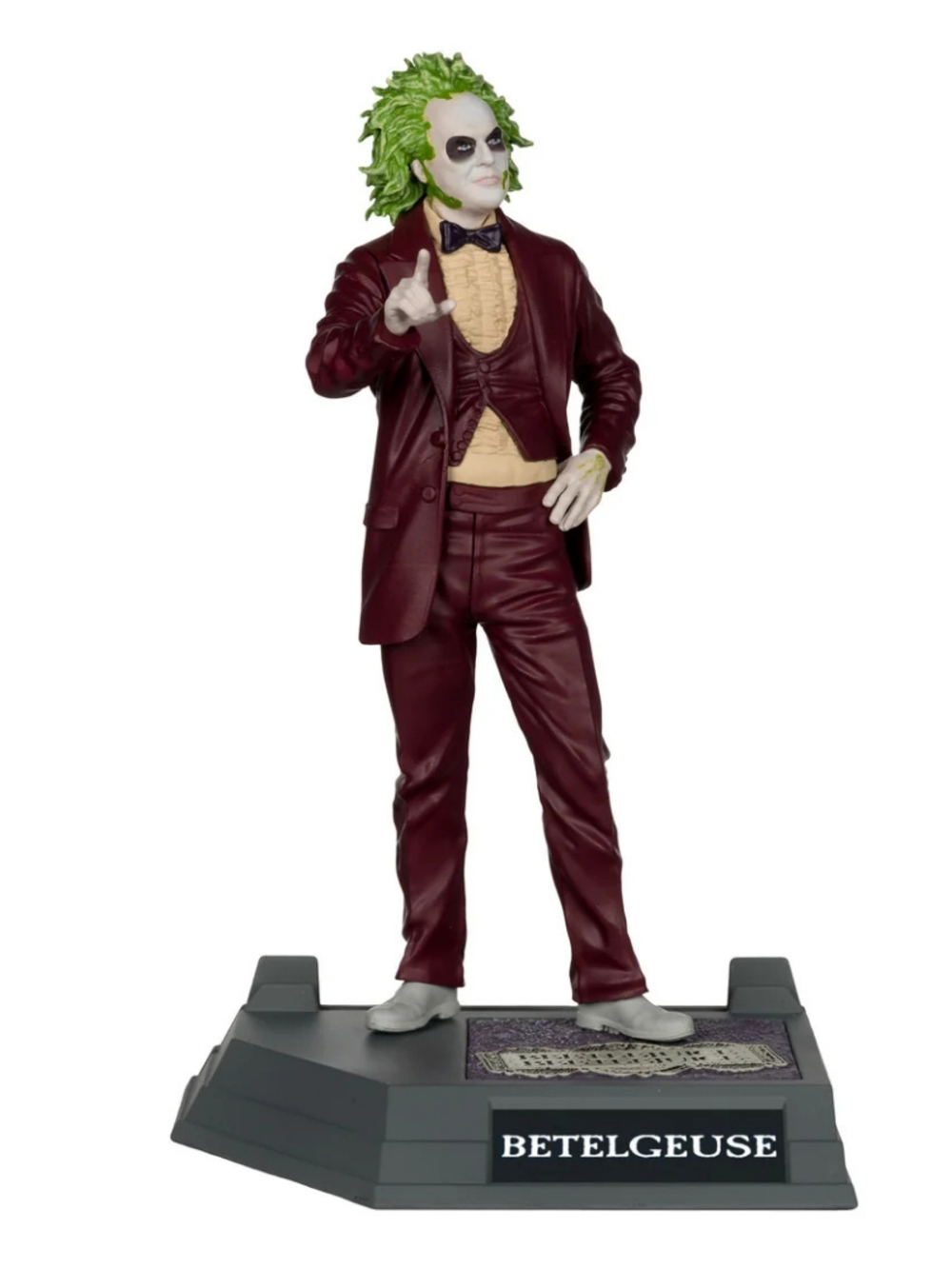 Bir Beetlejuice figürü, 'Beetlejuice' etiketli bir taban üzerinde duruyor. Bordo bir takım elbise, yeşil saç ve beyaz makyaj giyiyor.