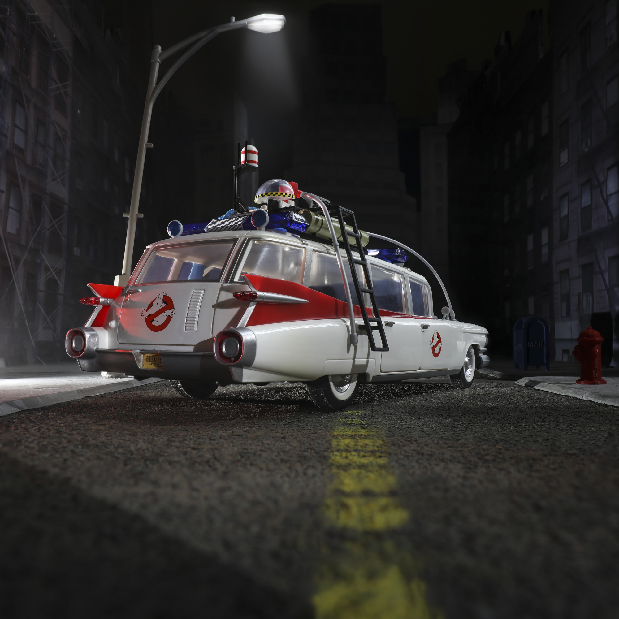 Gece şehir caddesinde, sokak lambası altında, Ghostbusters'tan beyaz ve kırmızı bir Ecto-1 oyuncak araba. Arka planda binalar.