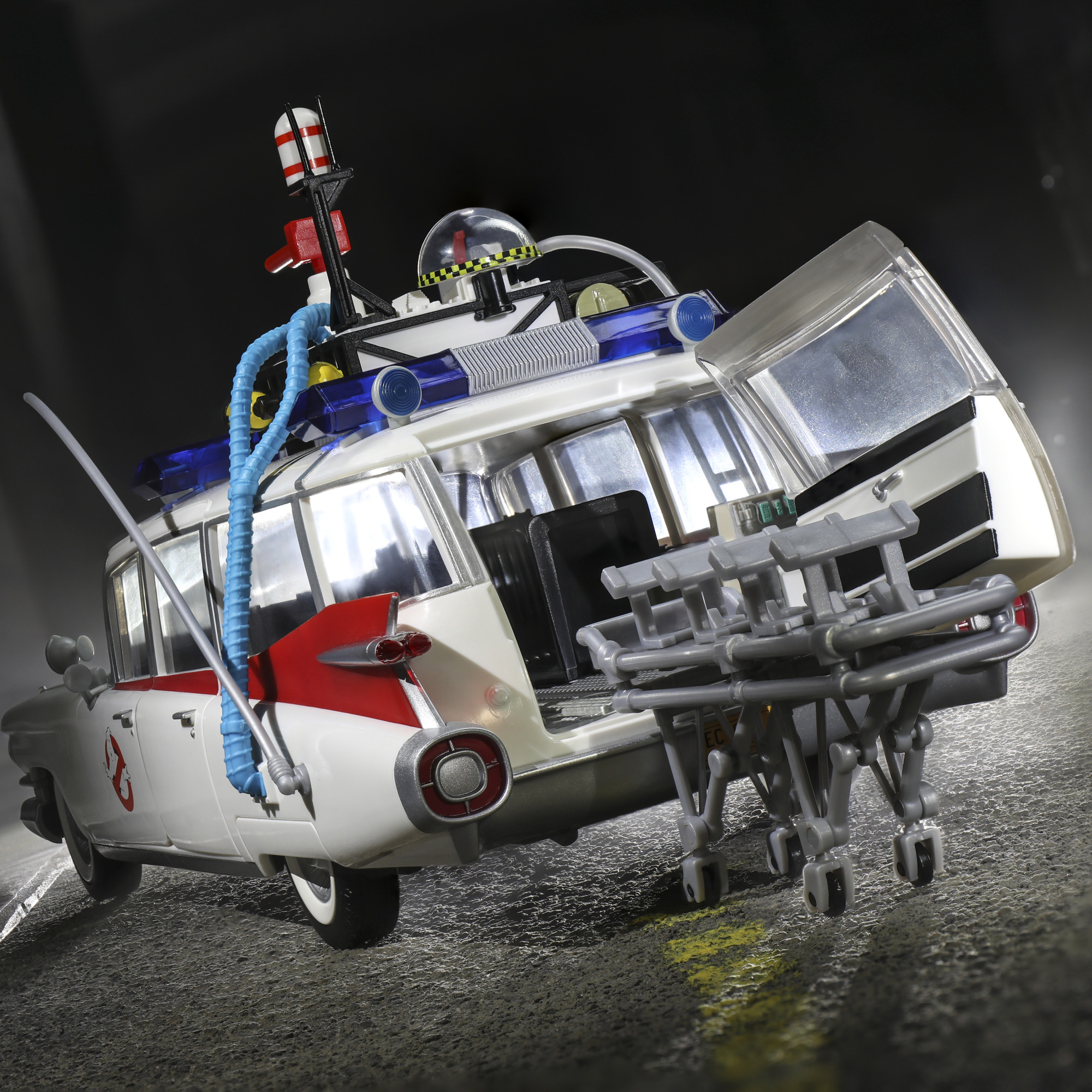 Bir Ghostbusters Ecto-1 oyuncak arabası. Beyaz gövde, kırmızı ve siyah detaylar. Üstte mavi hortum. İç mekanı ve ekipmanı gösteren açık arka kısım.