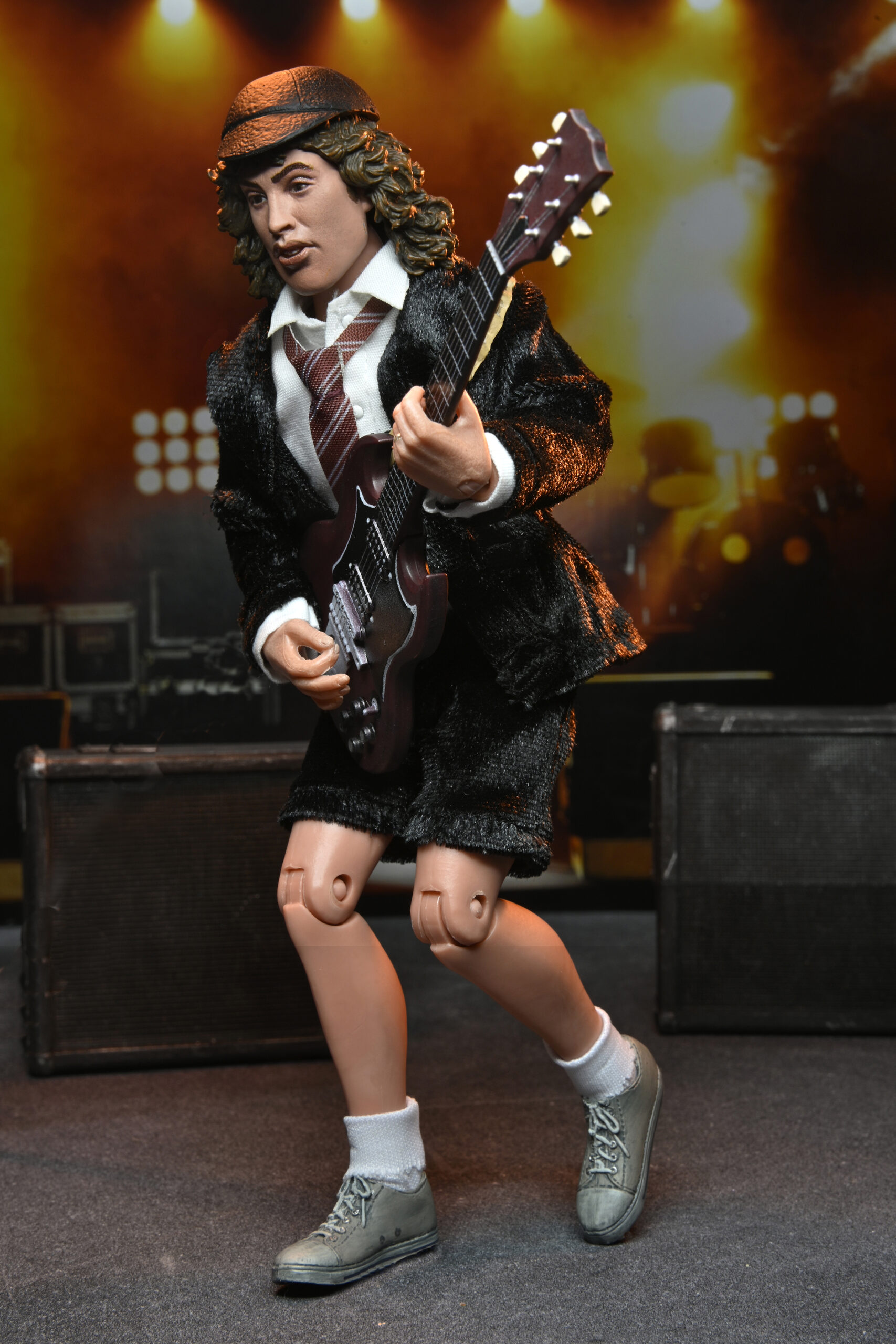 Sahne üzerinde gitar çalan takım elbiseli bir müzisyen figürü. Arka planda ışıklar ve hoparlörler.