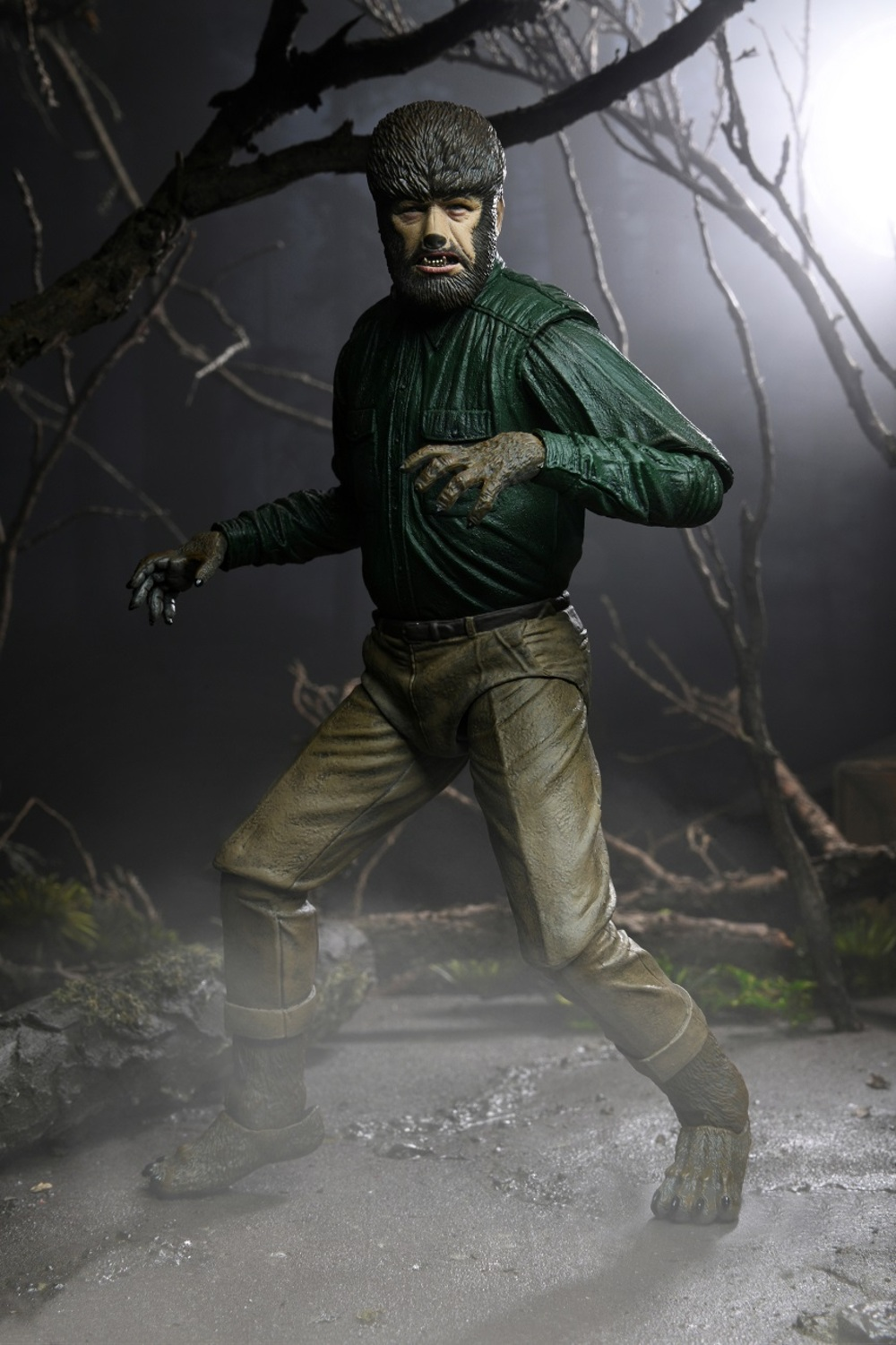 Una figura de hombre lobo se encuentra en un entorno forestal. Lleva una camisa verde y pantalones color canela. La figura tiene pelo en la cara y en las manos.