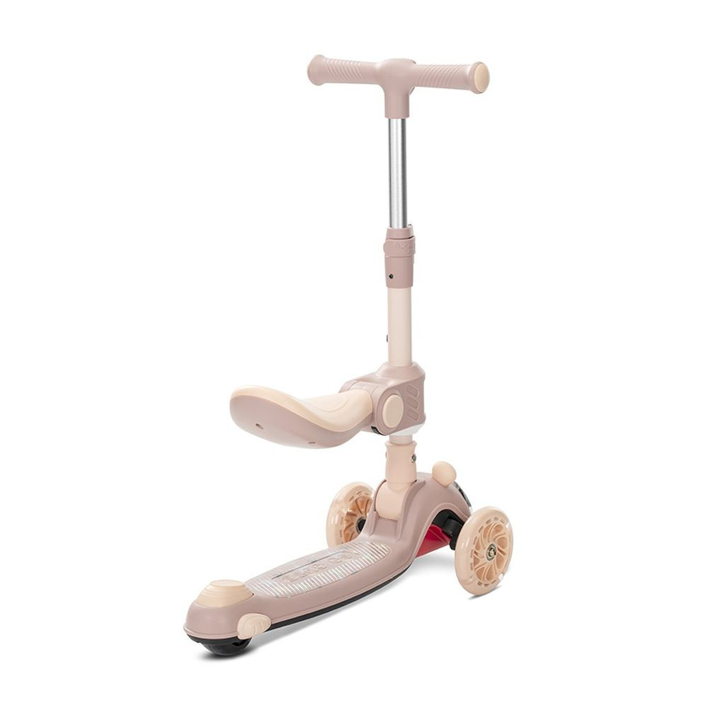 Un patinete beige y rosa con tres ruedas, un asiento y un manillar. Está sobre un fondo blanco.