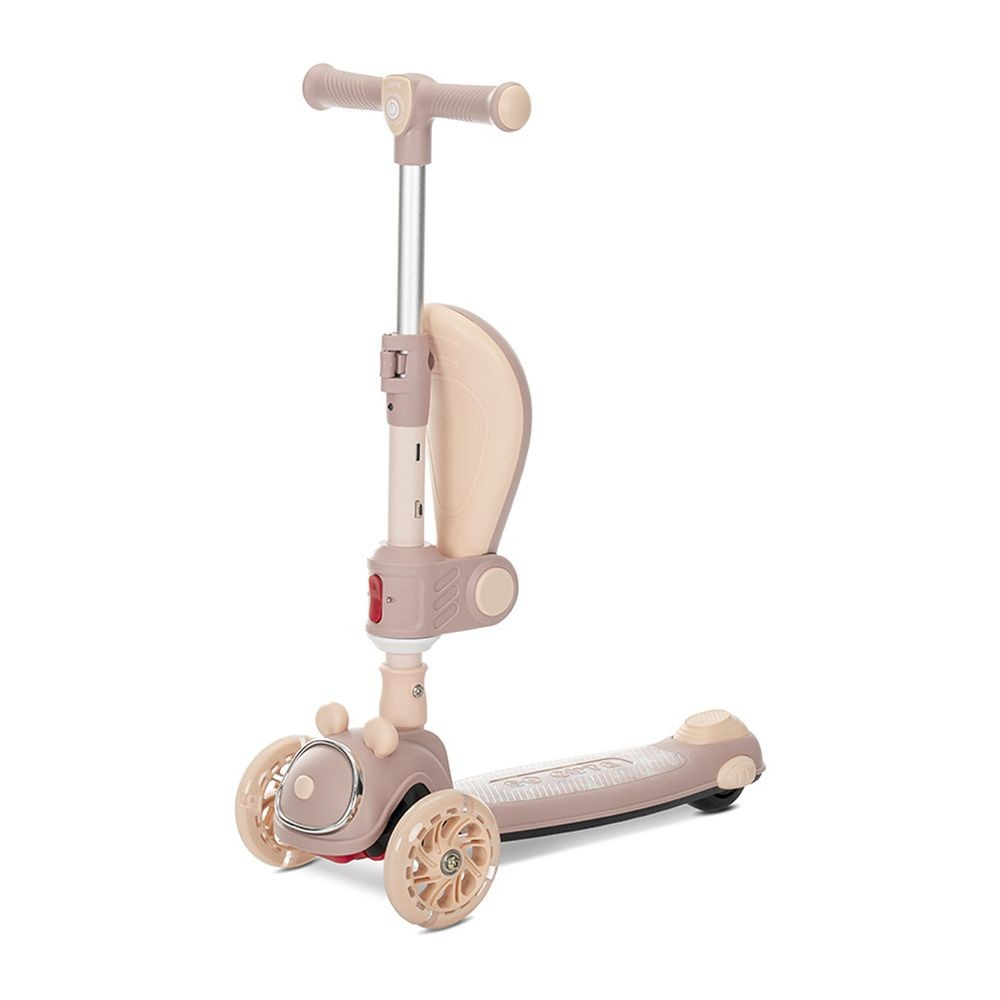 Un patinete de tres ruedas beige y rosa. Tiene manillar, asiento y plataforma. El patinete está sobre un fondo blanco.