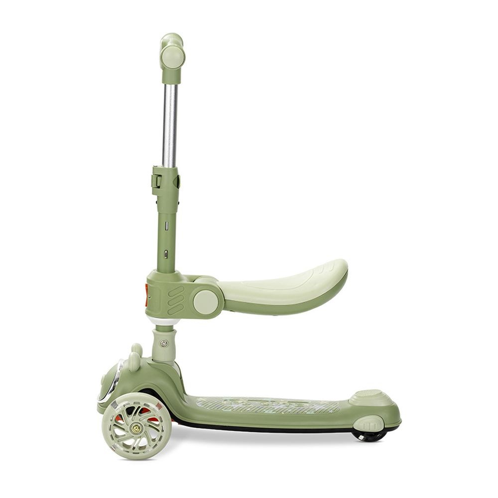 Un patinete verde con tres ruedas y un asiento sobre un fondo blanco. El patinete está orientado hacia la izquierda.
