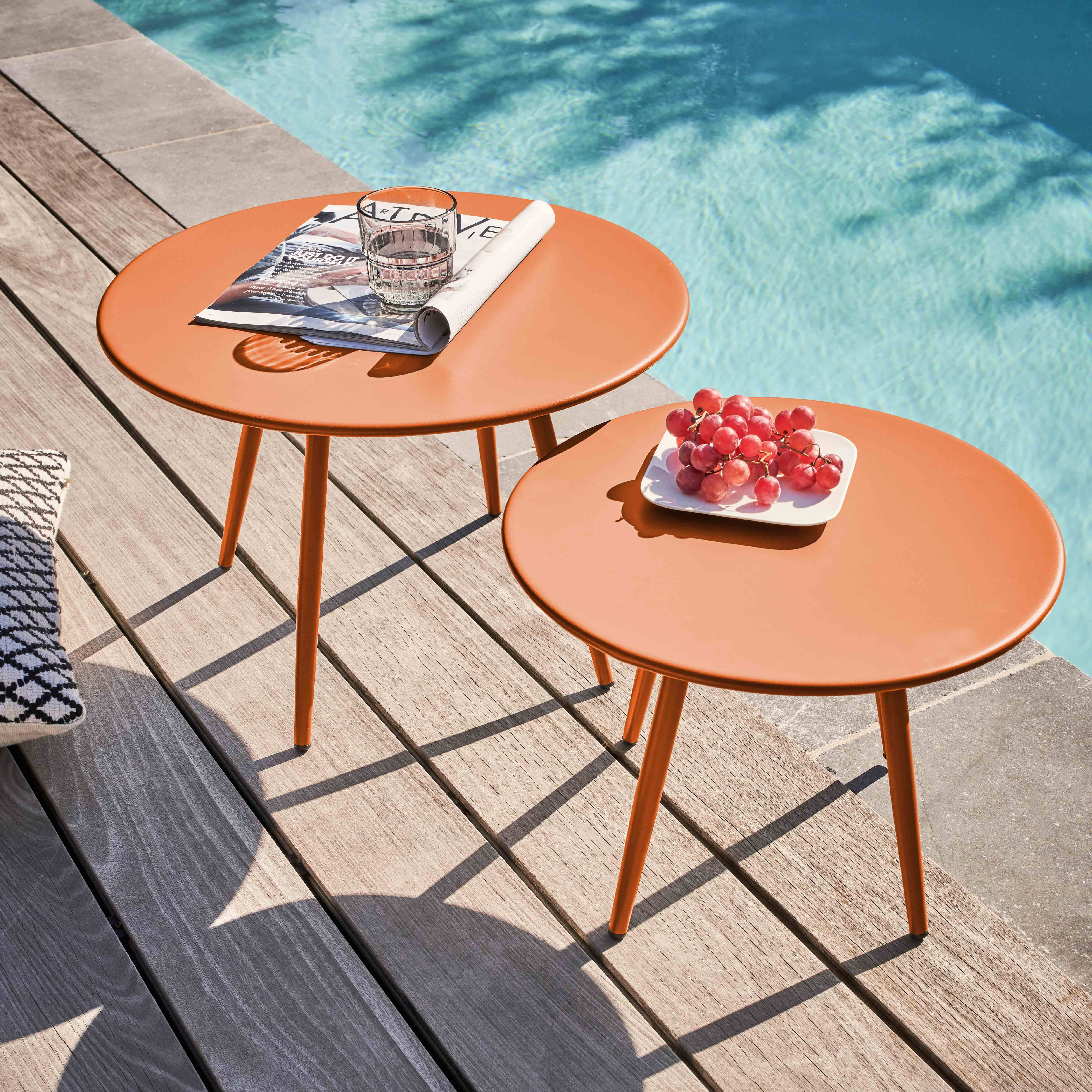 Zwei orangefarbene Tische neben einem Pool. Einer hat ein Glas und eine Zeitschrift. Ein anderer hat Trauben auf einem Teller.