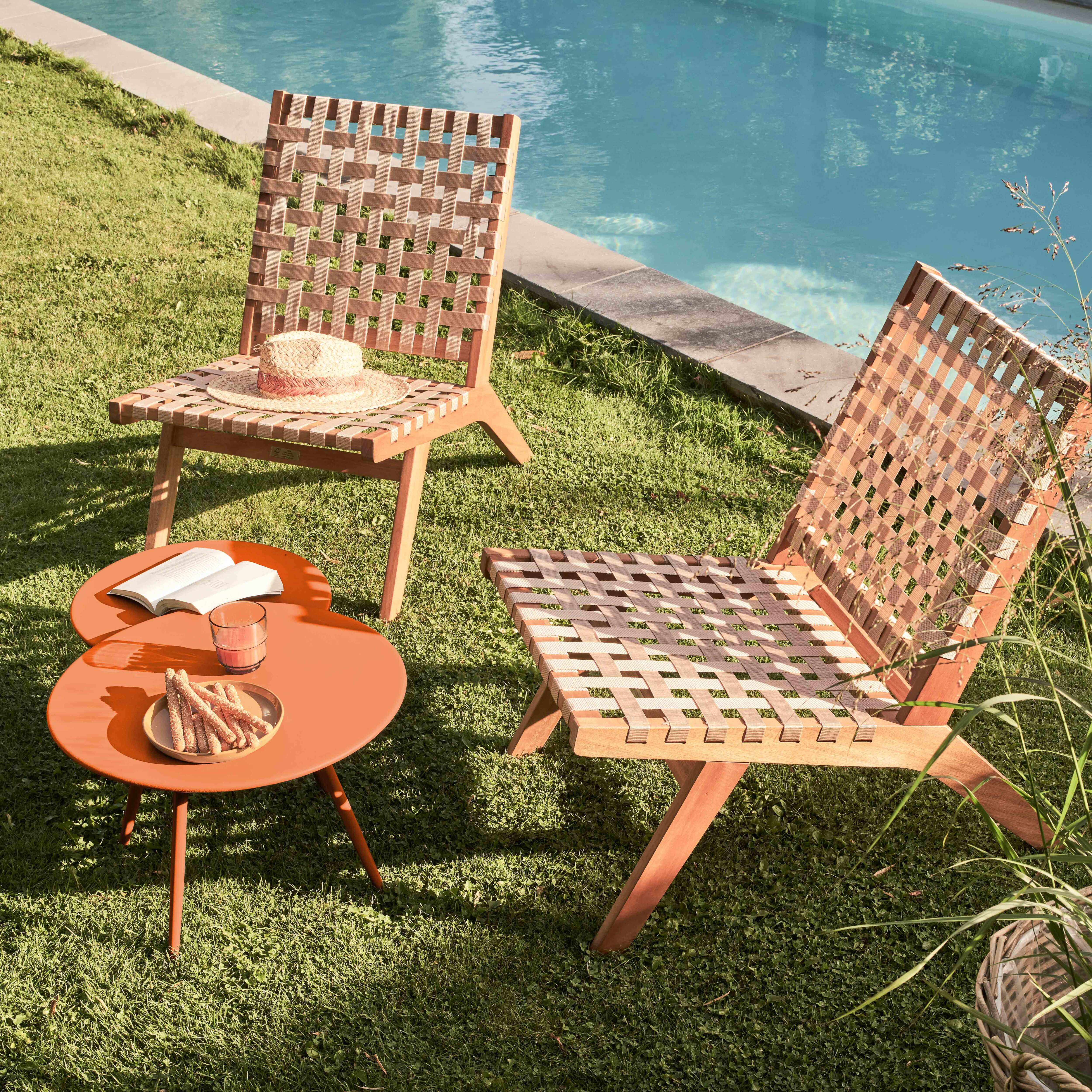 Zwei Stühle, ein Tisch mit Snacks und Getränken und ein Pool im Hintergrund. Auf einem Stuhl liegt ein Strohhut.